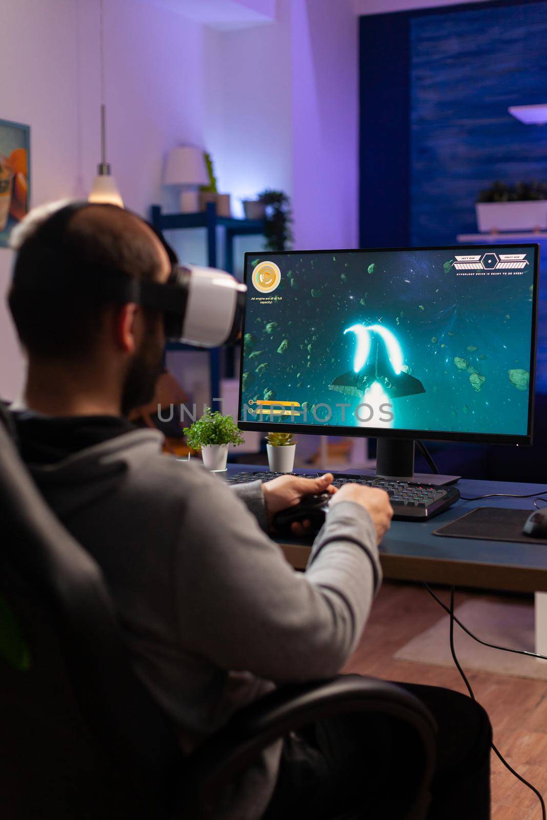 Player man playing video game at powerful computer late night wearing vr headset. Excited player using wireless controller for virtual tournament gaming space shooter at home
