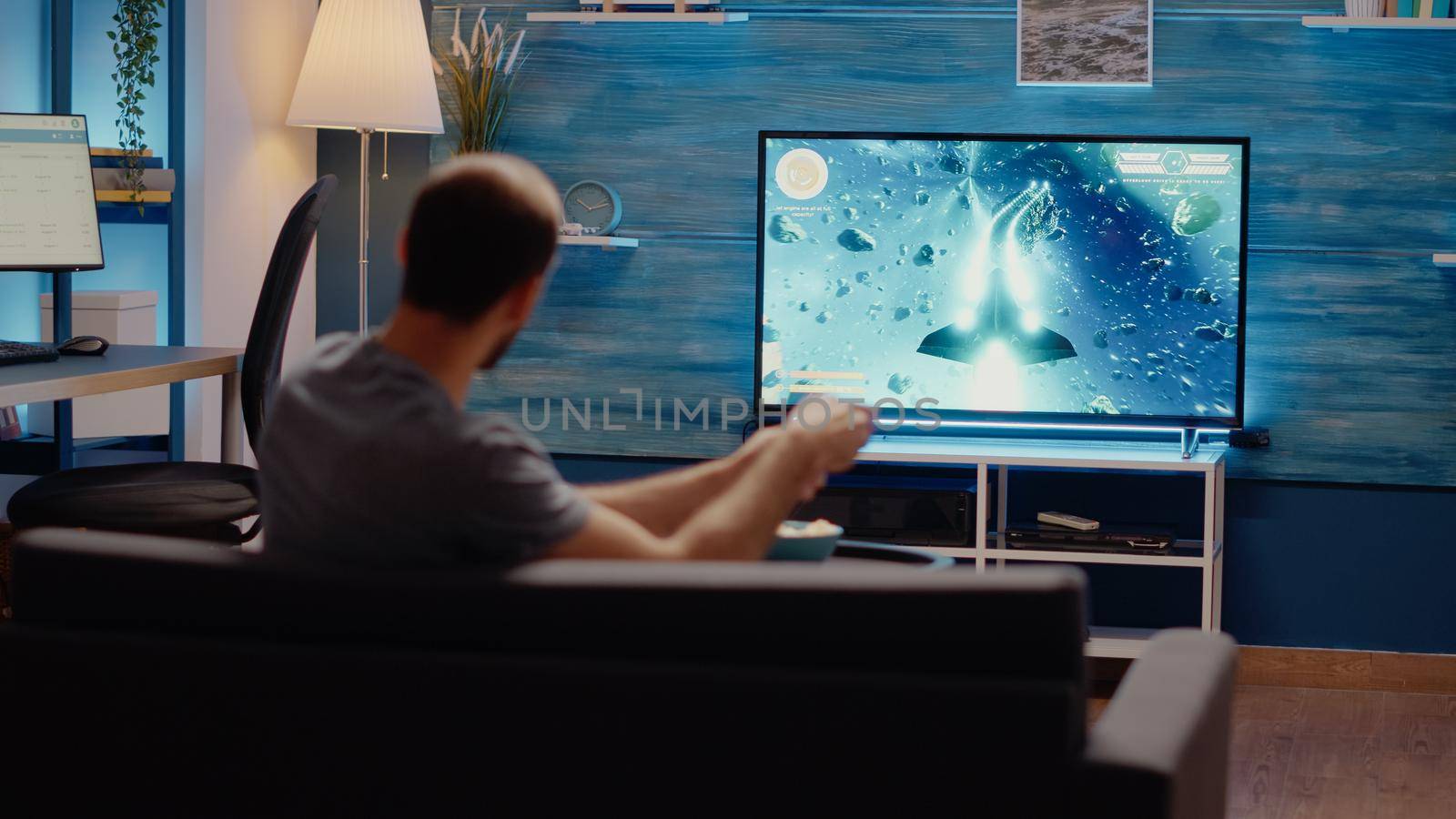 Young man with online console playing video games indoors while holding controller for action competition. Person using television and joystick for virtual electronic entertainment