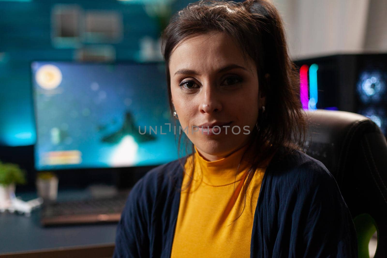 Portrait of woman gamer looking into camera after playing space shooter games using professional RGB keypad on powerful computer. Caucasian pro player streaming online videogames in home studio