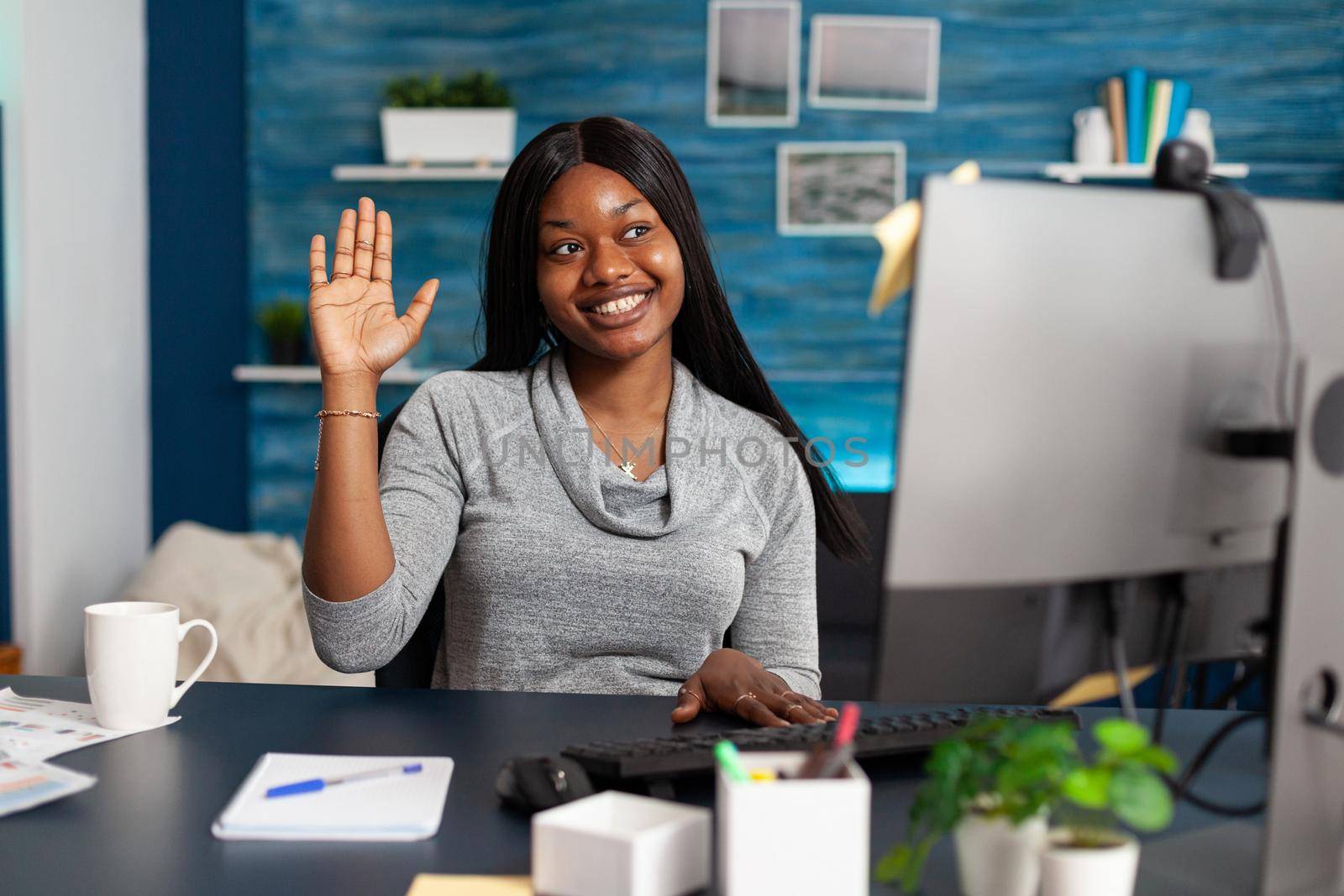 Student with dark skin waving university teacher during online videocall meeting by DCStudio