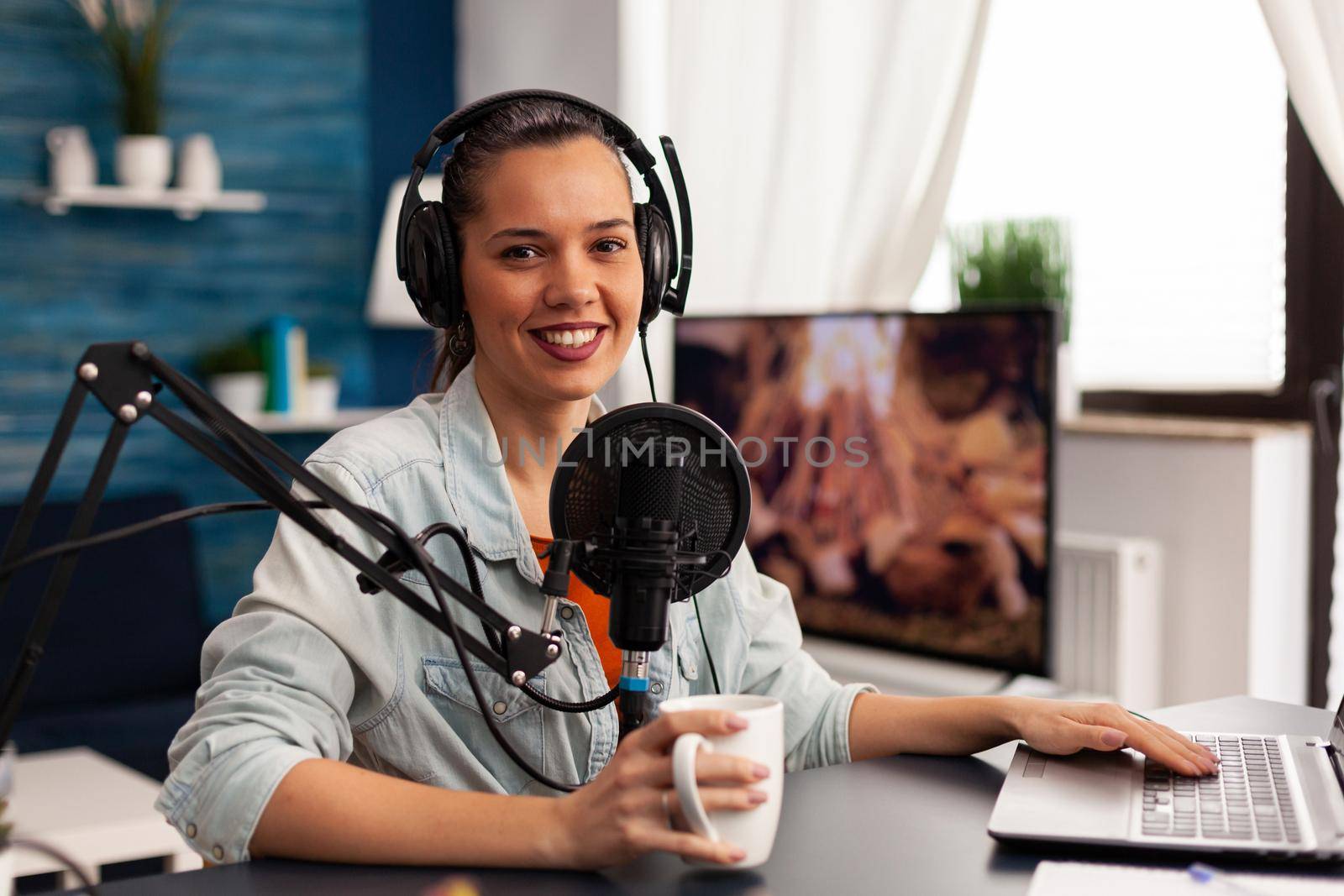 Smiling influencer woman sitting in front of camera recording video for fashion blog. Digital blogger vlogger streaming talk show in studio using headphones, professional podcast microphone