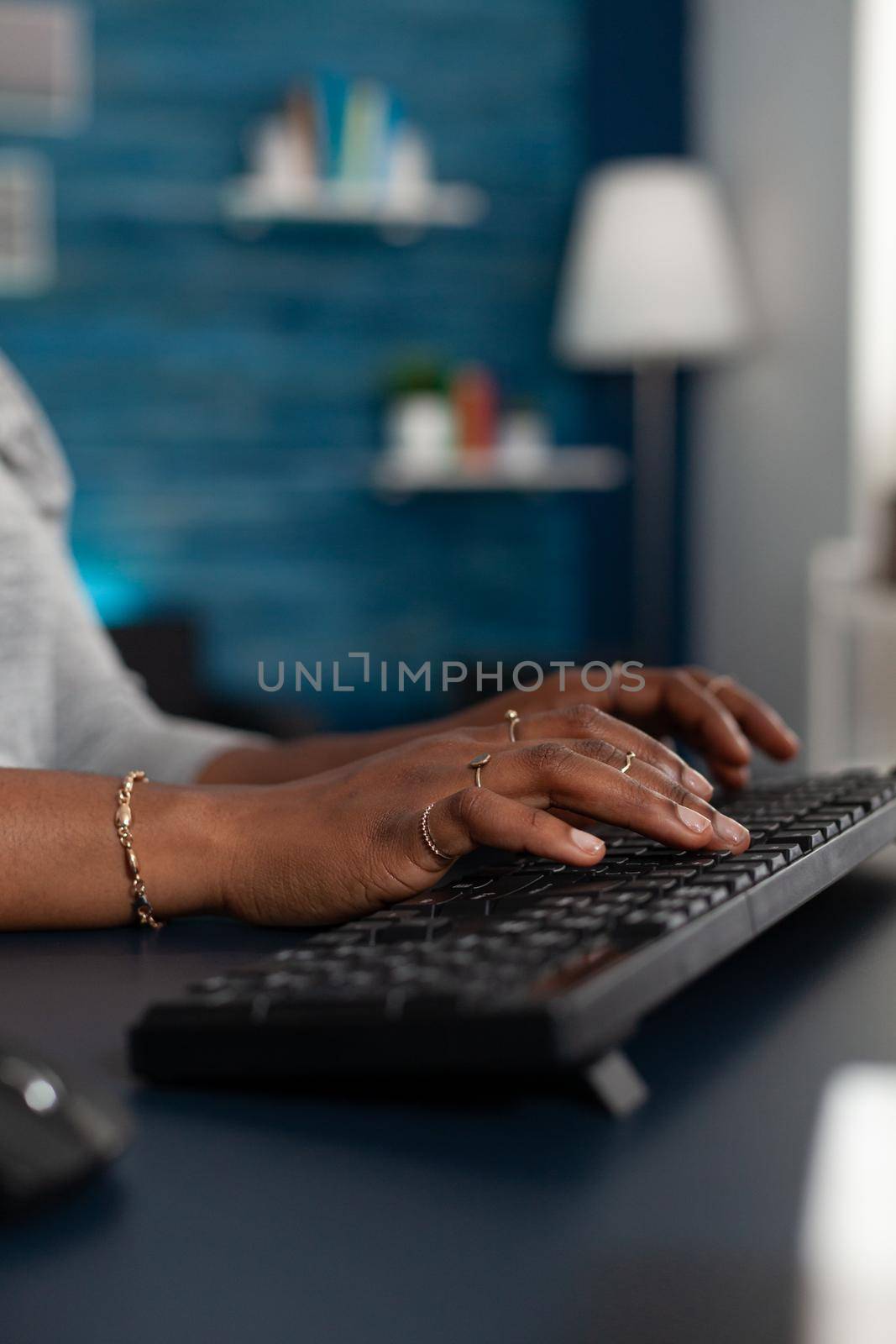 Close-up of black student hands typing on keyboard browsing online information on internet working remote at business article sitting at desk table. African american woman searching education email