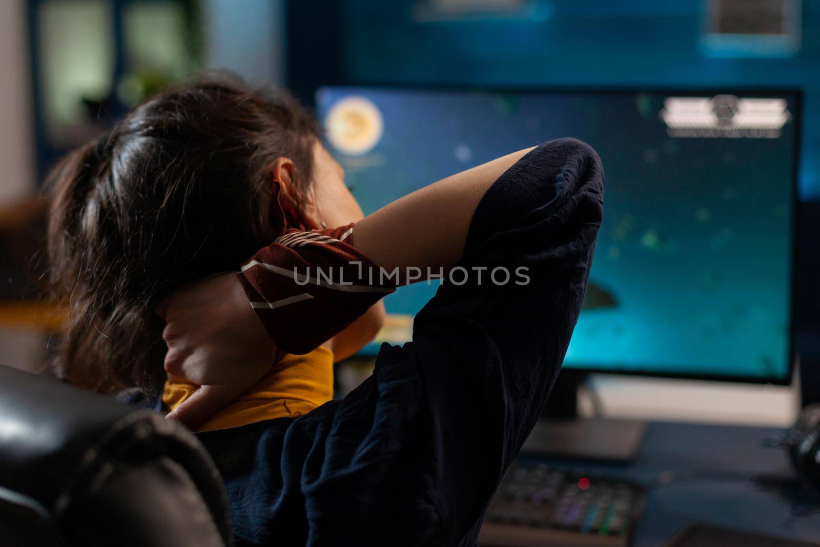 Woman player streatching neck before started playing online videogames on powerful computer in gaming studio. Excited player sitting on gaming chair streaming video games using RGB keyword