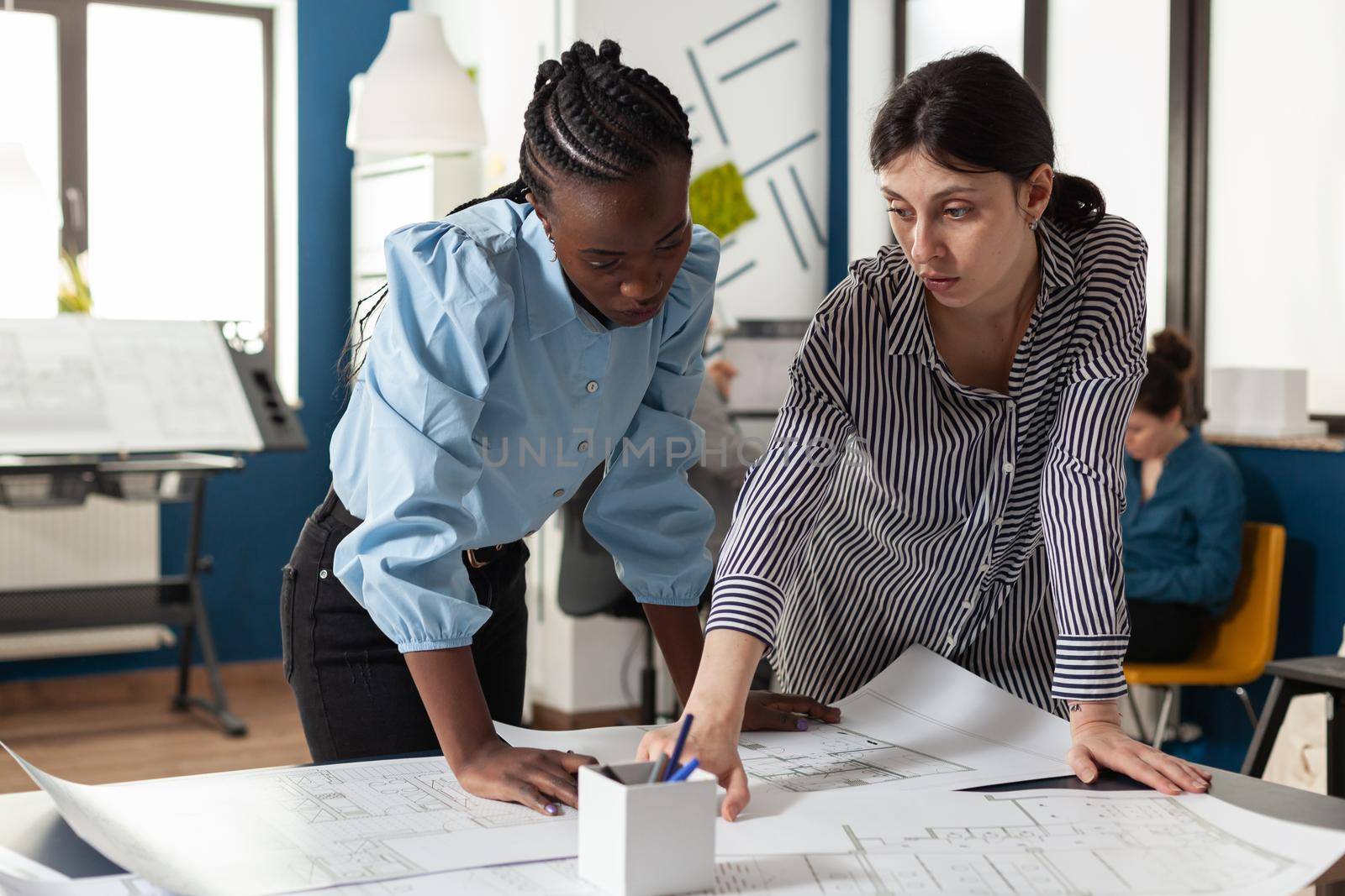 Architectural team of multi ethnic women plan sketch blueprint layout for design project building model maquette. Diverse group pointing at construction on paper for job occupation