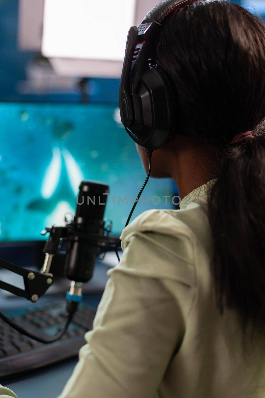 Dark skinned online e sport player talking into microphone with teammates. Streaming viral video games for fun using headphones and keyboard for online championship.