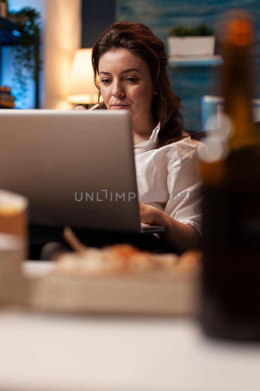 Woman relaxing on sofa eating tasty snack while watching comedy movie film on laptop computer late at night in living room. Caucasian female enjoying takeaway food home delivered. Fastfood order