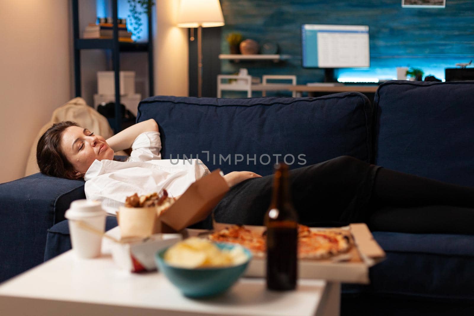 Caucasian female falling asleep after eating junk-food in living room late at night by DCStudio