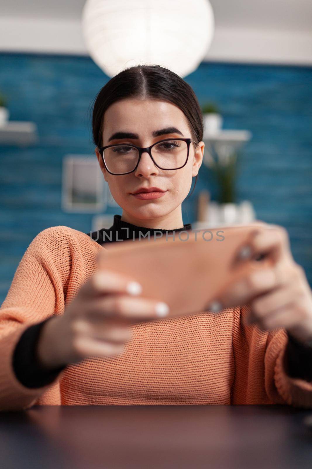 Gamer playing online videogames during shooter competition on modern smartphone. Competitive digital player at desk table in living room during online mobile gaming tournament