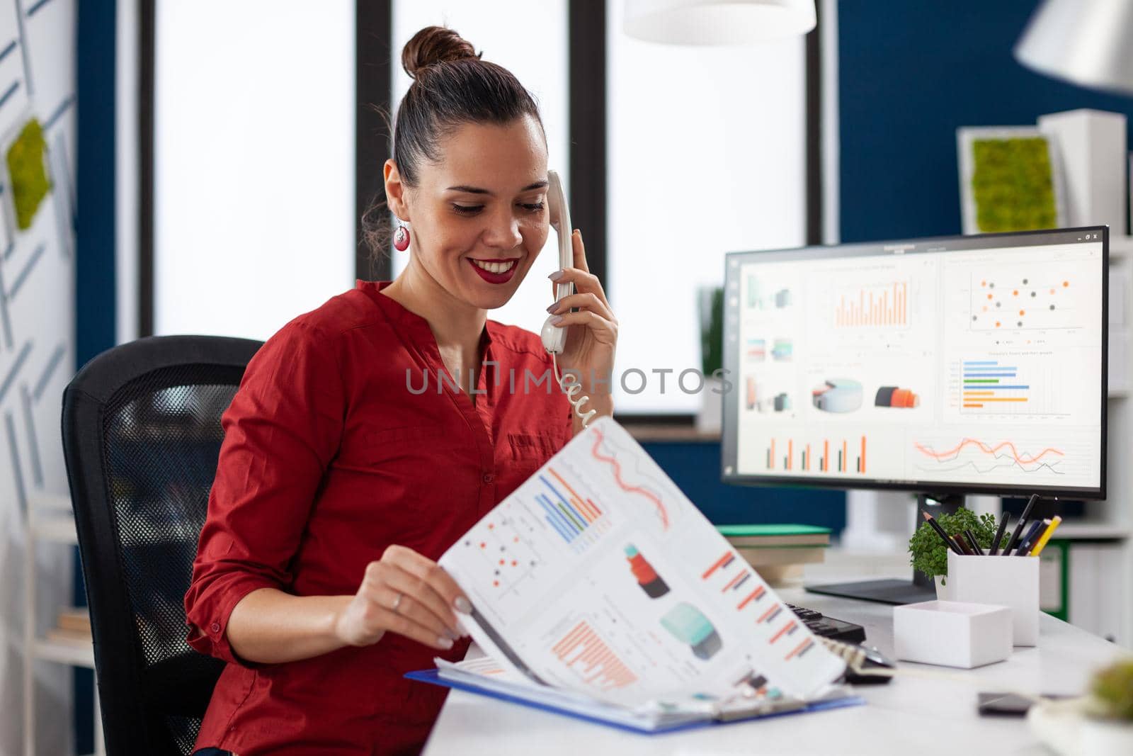 Businesswoman in company office checking finaicial statistics on clipboard, discusing details with coworkers during phone call conversation. Happy entrepreneur communicating with client.