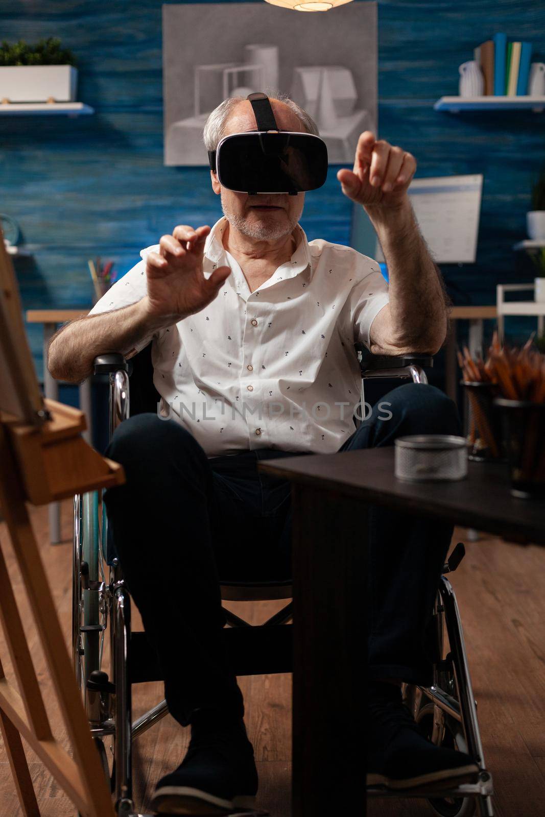 Invalid aged artist using vr glasses to draw masterpiece design on canvas and easel at fine art studio. Disabled senior man with modern headset sitting in wheelchair, for drawing hobby