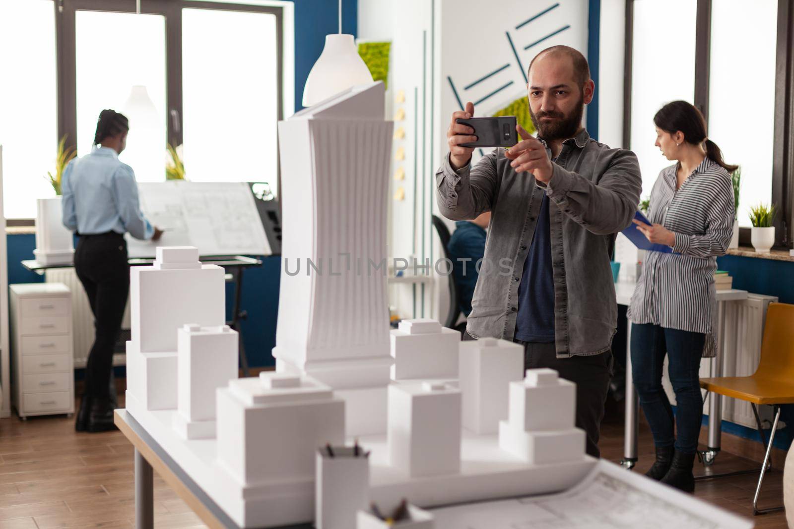 Architect profession man looking at maquette layout using smartphone to design building model plan maquette. Urban designer constructor working on professional modern construction