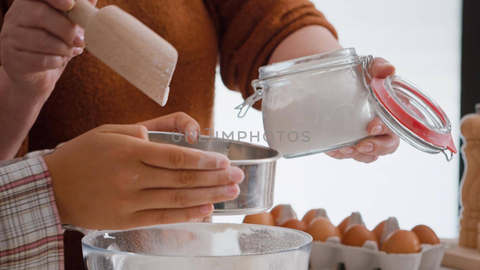 Closeup of grandmother putting flour ingredient in strainer while grandchild preparing traditional winter cookie in culinary kitchen. Family enjoying christmas holidays making homemade dessert