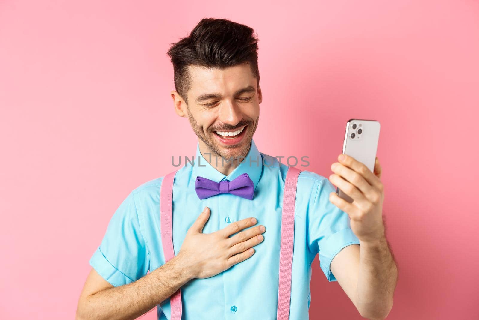 Image of handsome guy laughing during video chat, having mobile conversation and chuckle from something funny, standing on pink background by Benzoix