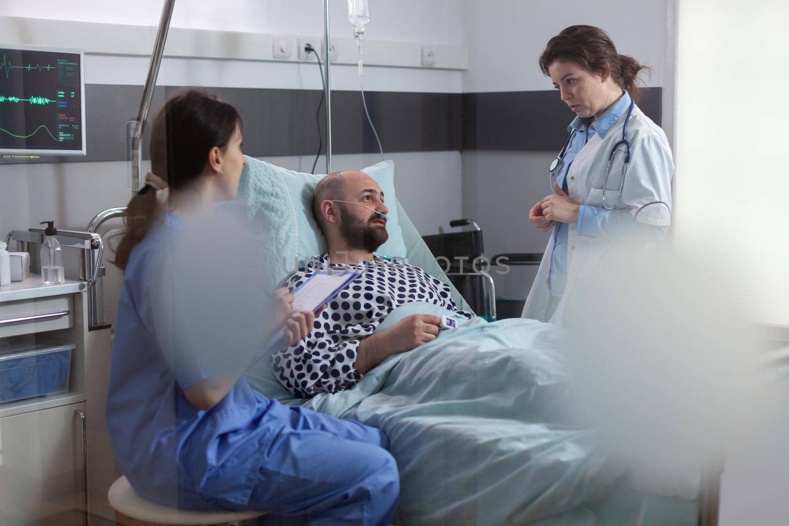 Medical team monitoring sick man explaining disease symptom examining medical recovery in hospital ward. Patient sitting in bed waiting specialist treatment during rehabilitation appointment