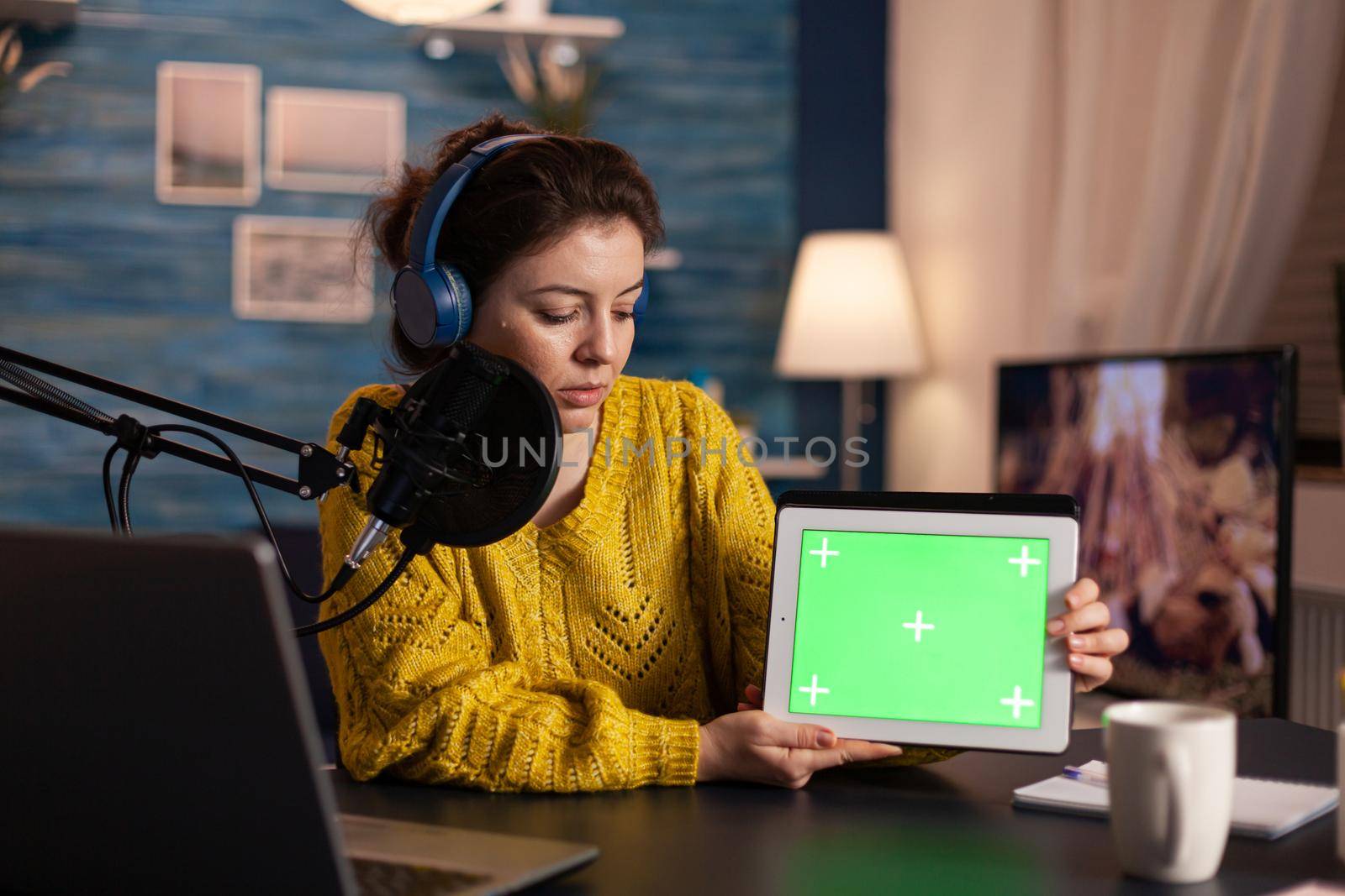 Vlogger looking at laptop and talking about tablet with chroma key desktop. On-air production internet broadcast host streaming live content using mochup, green screen, izolated desktop.