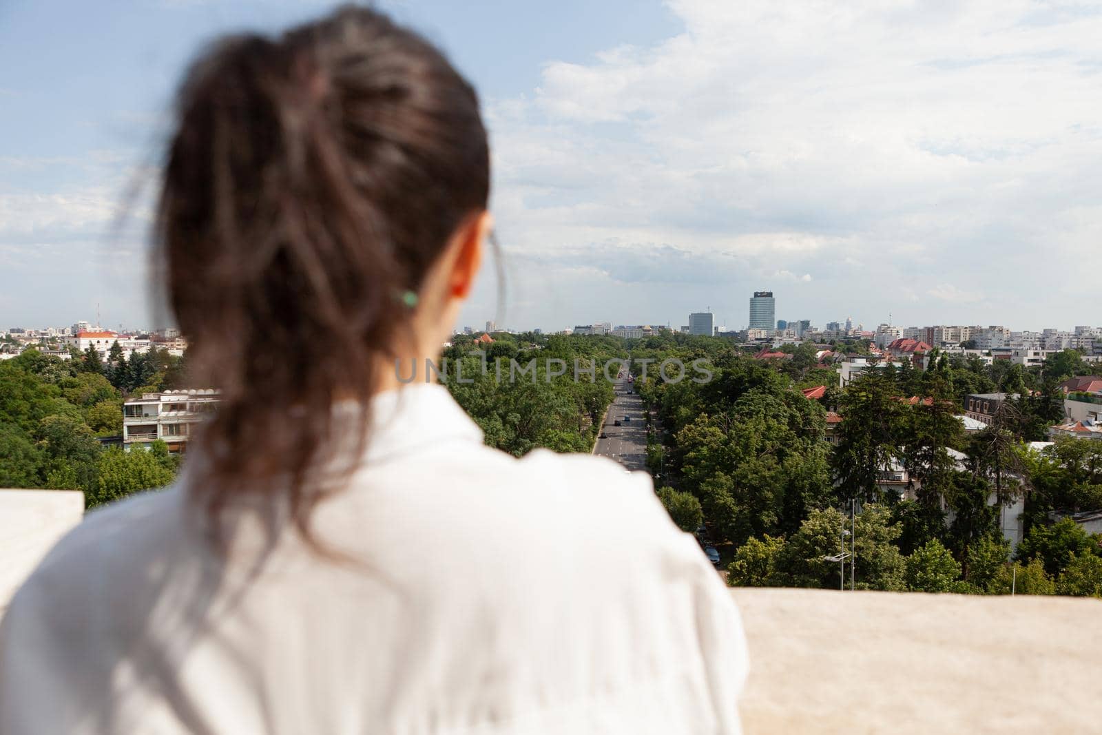 Back front of caucasian female toursit standing on tower terrace enjoying seeing panoramic view of metropolitan city during summer vacantion. Landscape with urban skyscraper rooftop and aerial view