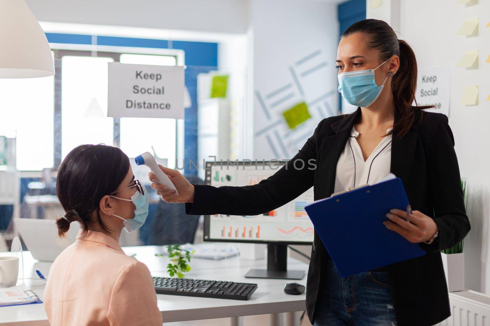 Company worker keeping social distancing scanning colleague temperature with infrared themermoter to prevent infection with virus during global pandemic with covid-19. Checking healthcare of office worker for fever.