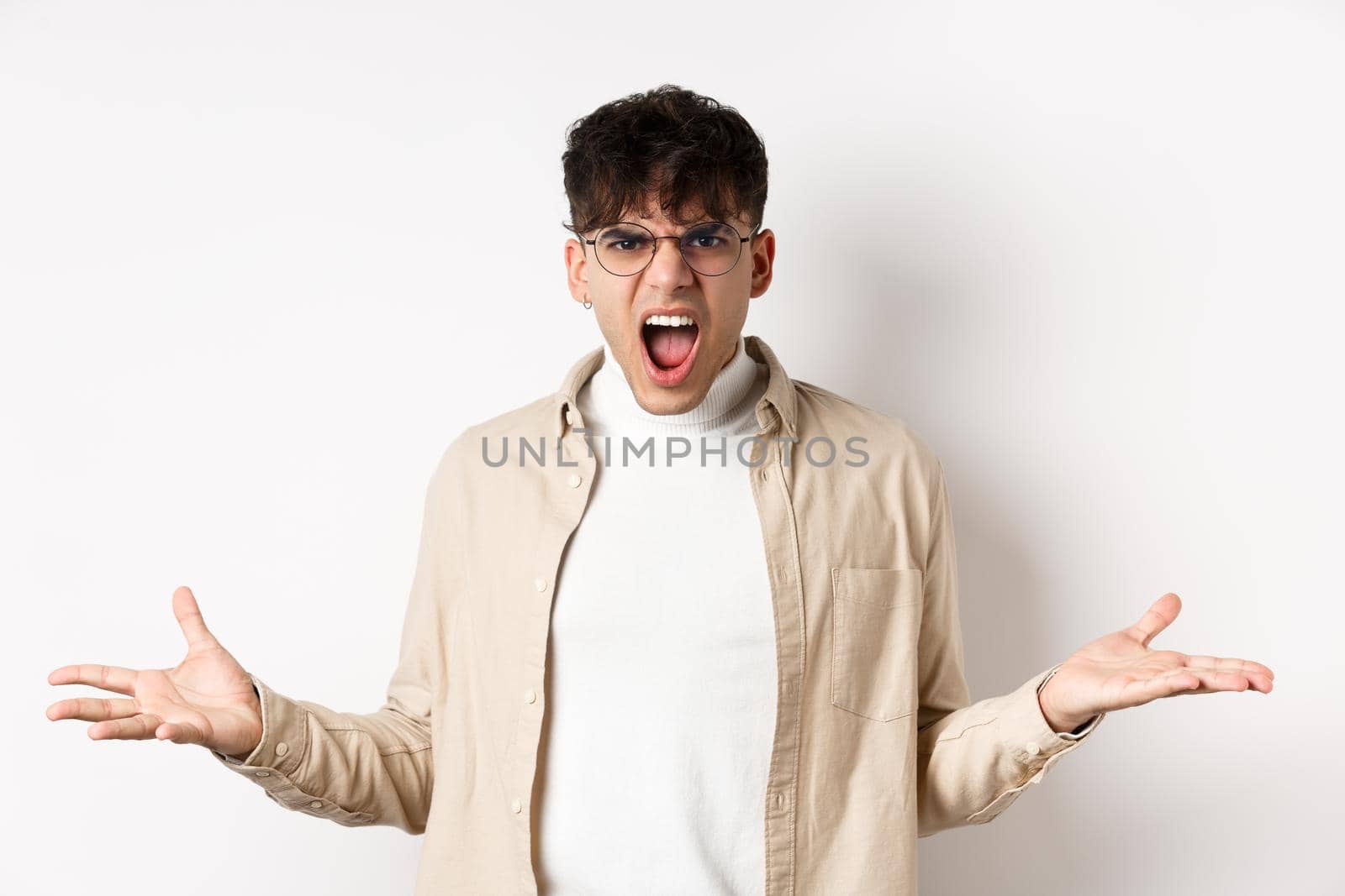 Portrait of angry frustrated man shouting and having argument, spread hands sideways and grimacing outrated, standing pissed-off on white background.