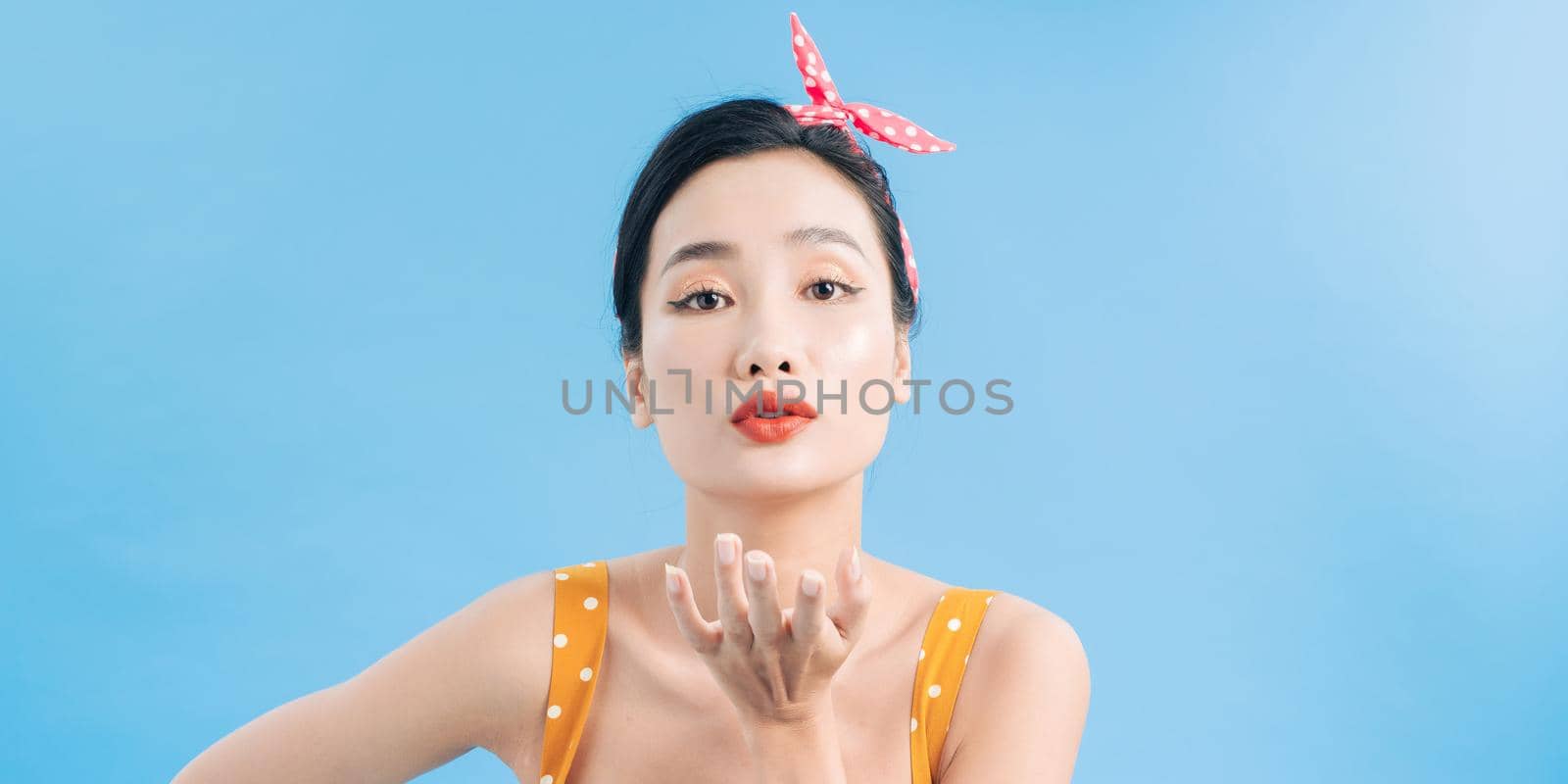 Picture of Pleased asian woman sends air kiss at the camera over blue background