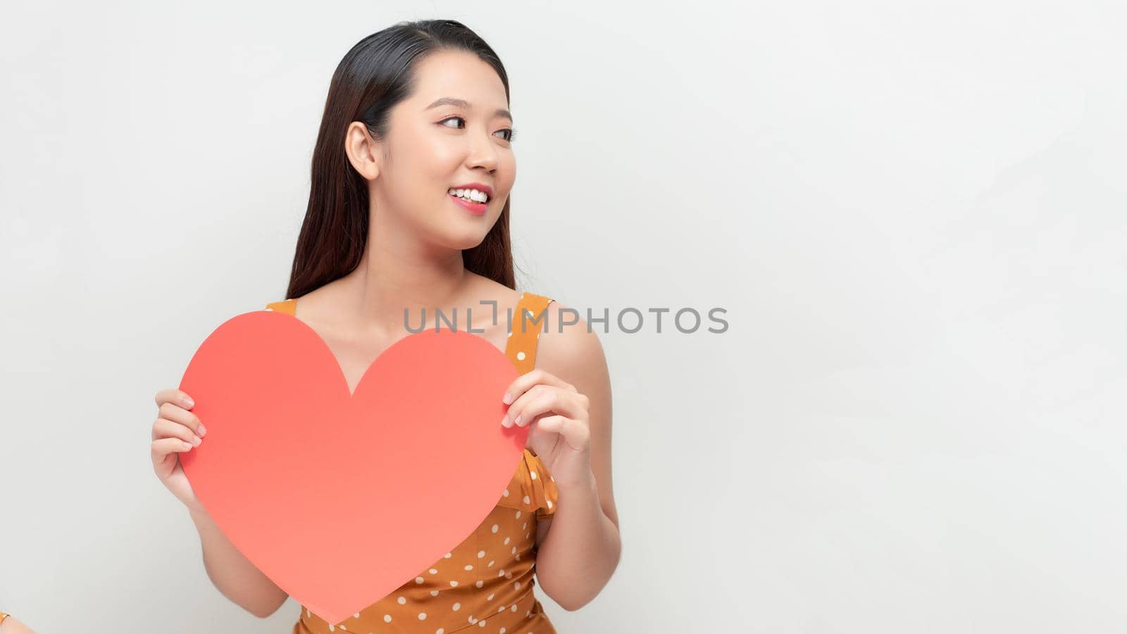Smiling  asian girl holding big red heart shape, and looking away