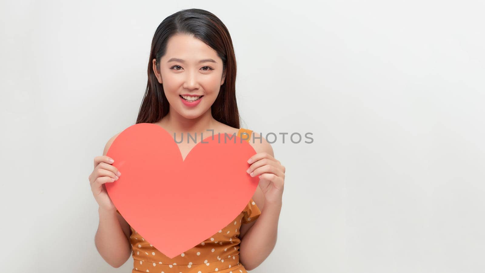 Attractive young smiling woman holding big red heart in hands isolated on white background. 