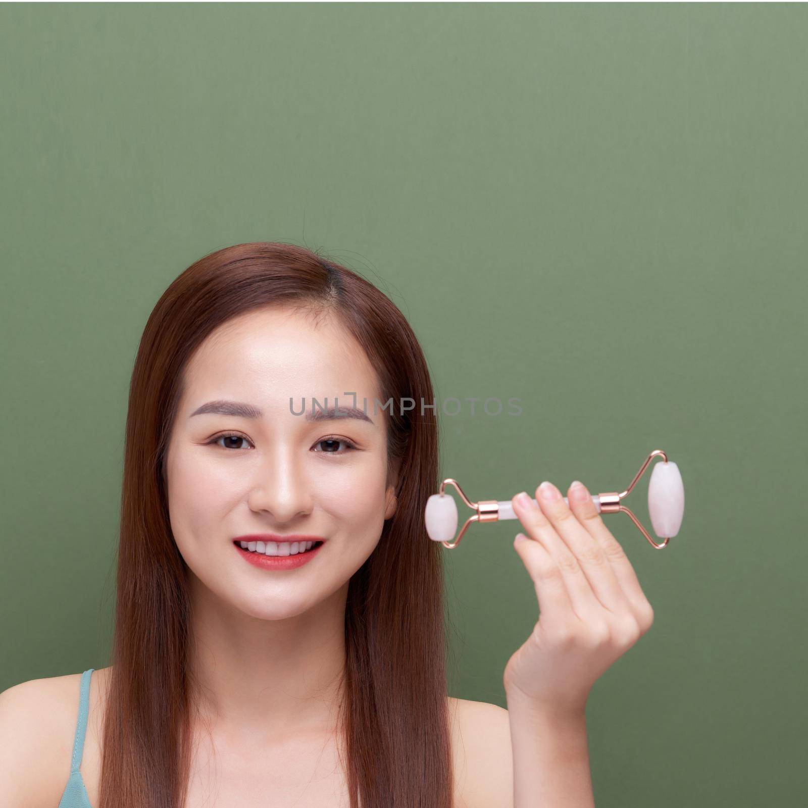 Portrait photo of a young woman looking relaxed use while using a natural pink quartz face roller by makidotvn