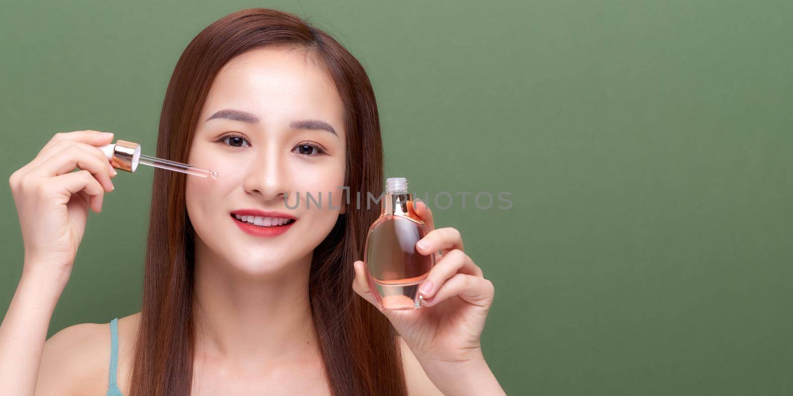 Smiling woman holding vitamin c serum near her face on green background