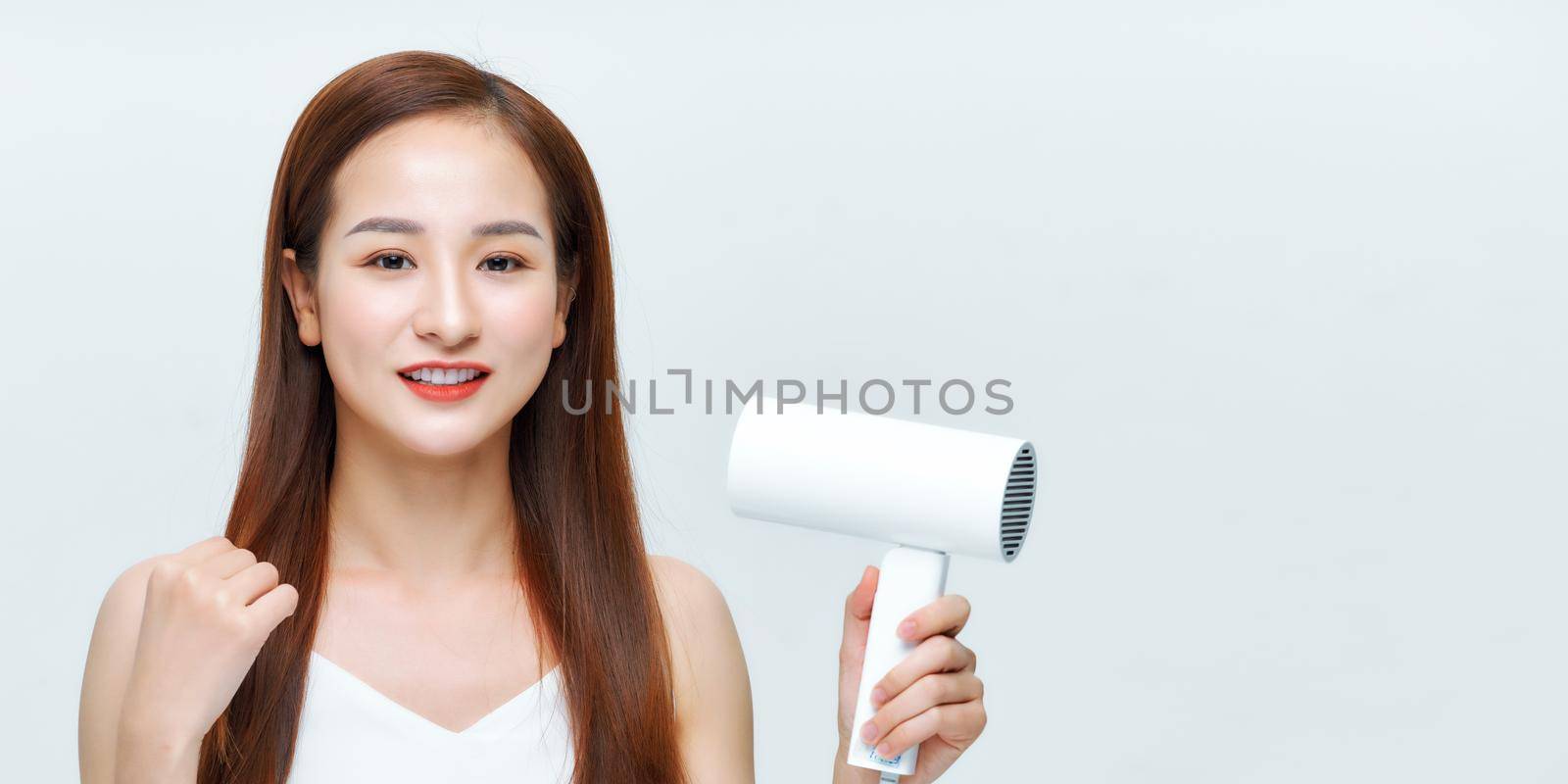 young woman makes hair volume with hairdryer in hand on white background