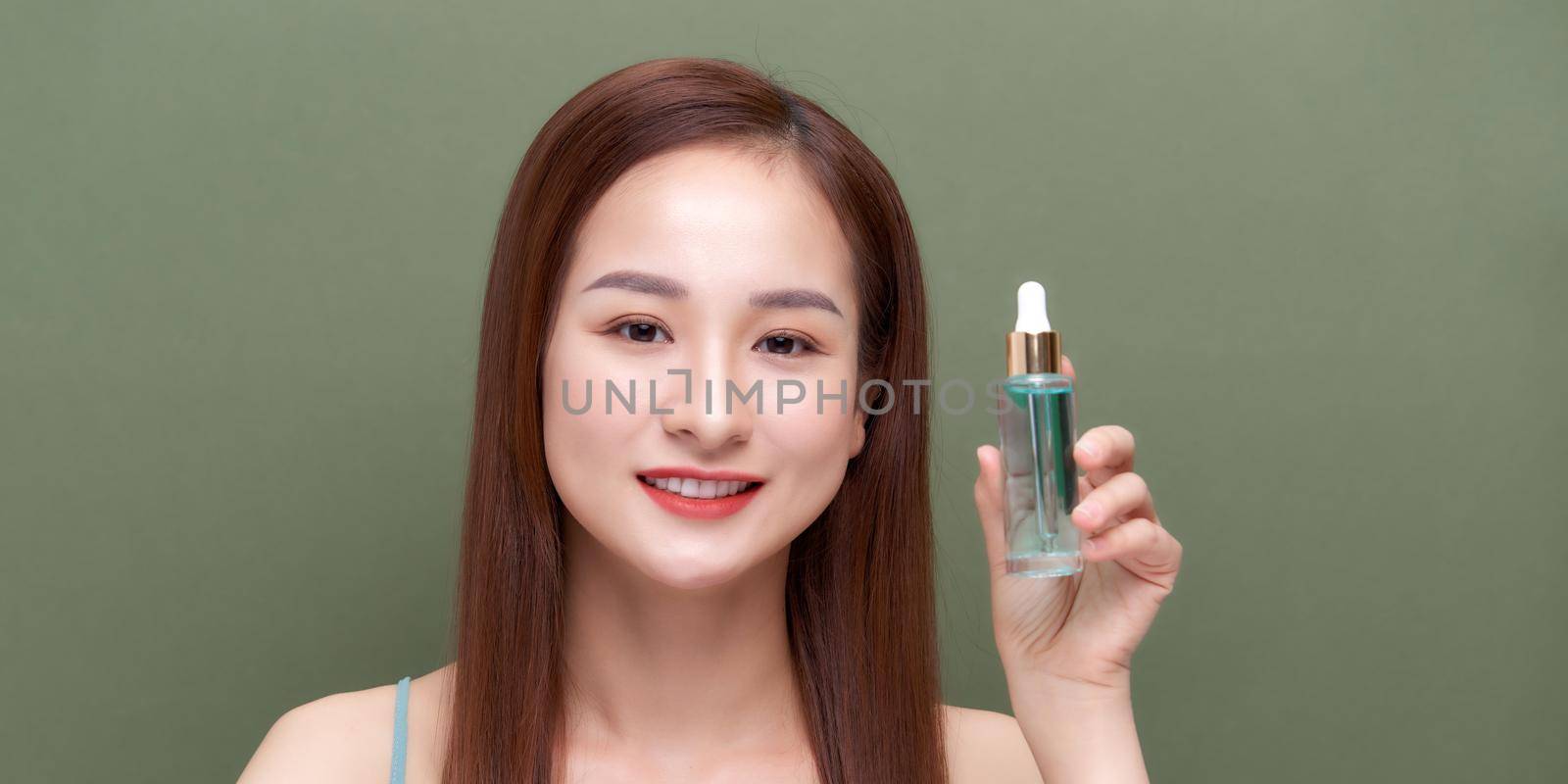Smiling woman holding vitamin c serum near her face on green background by makidotvn