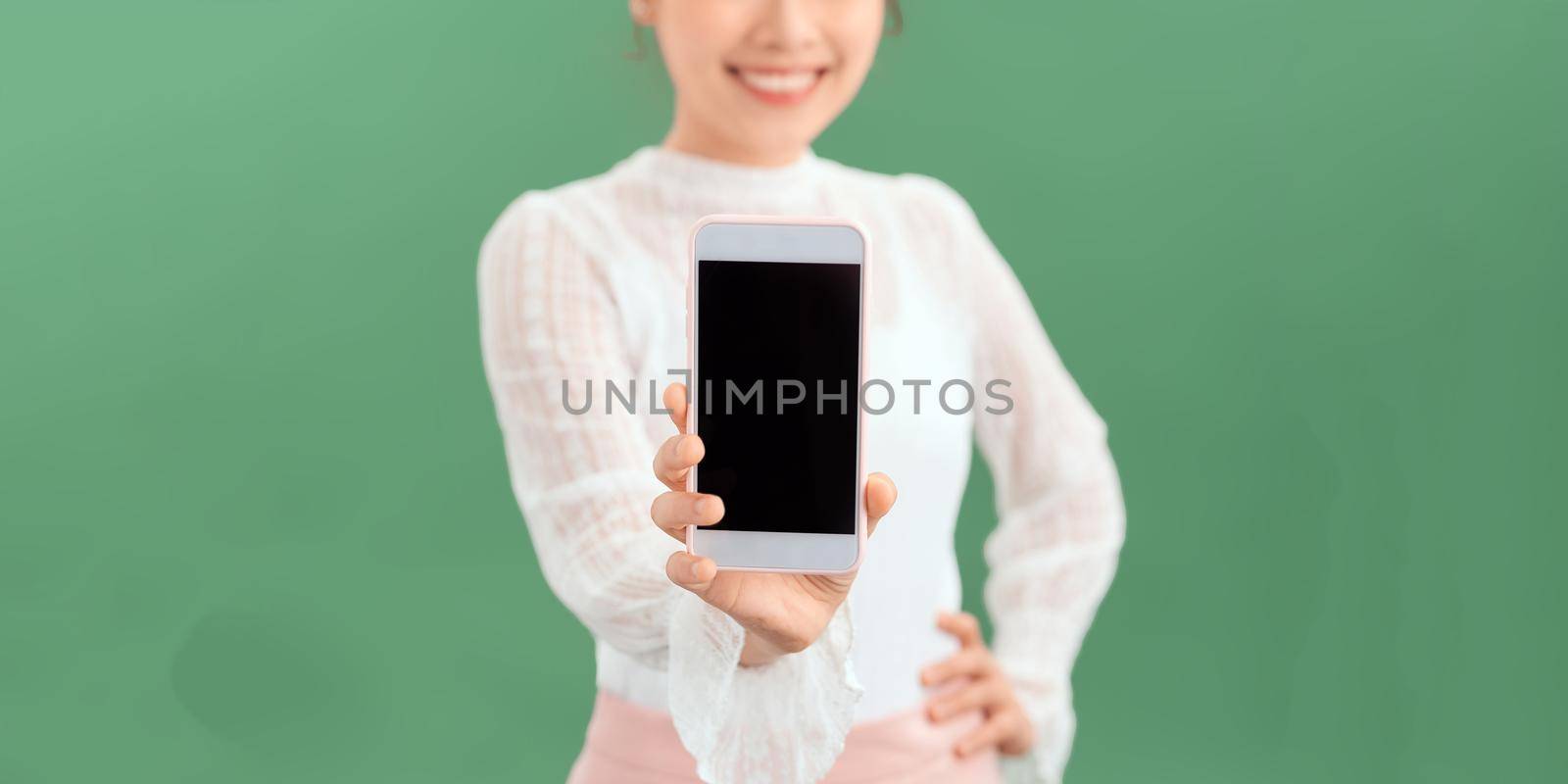 Portrait of smiling young woman holding mobile phone with blank empty screen isolated on green background