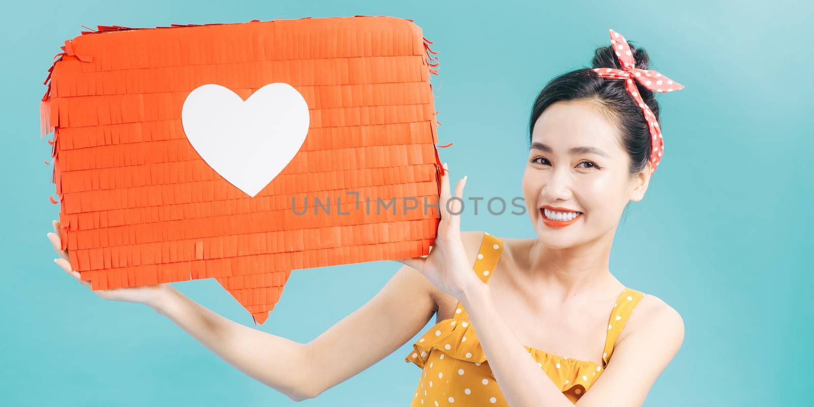 pretty smiling girl holding red paper with heart symbol and looking at camera isolated on blue