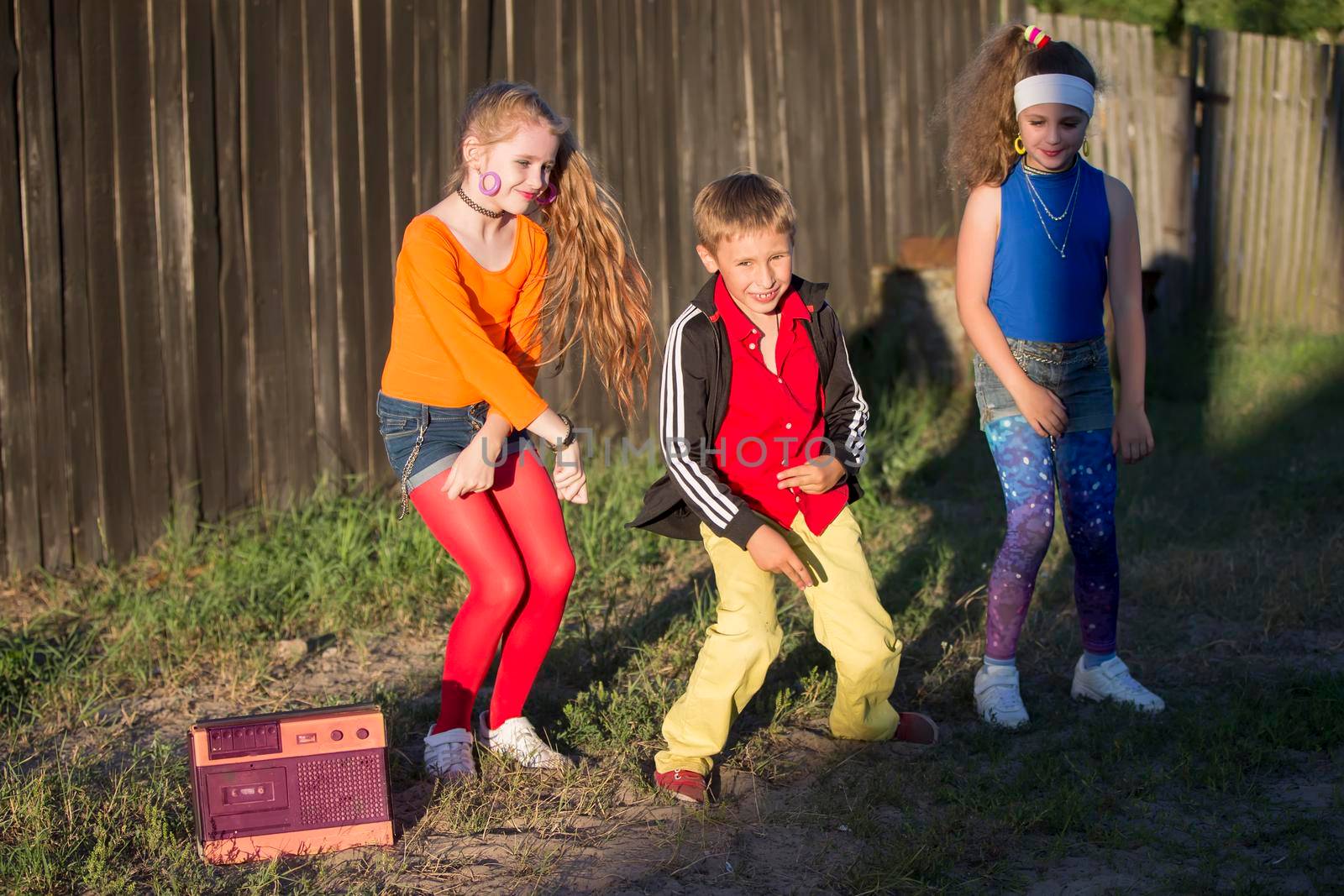 Retro kids. Two girls mi boy dressed in the style of the nineties are dancing to a retro tape recorder.