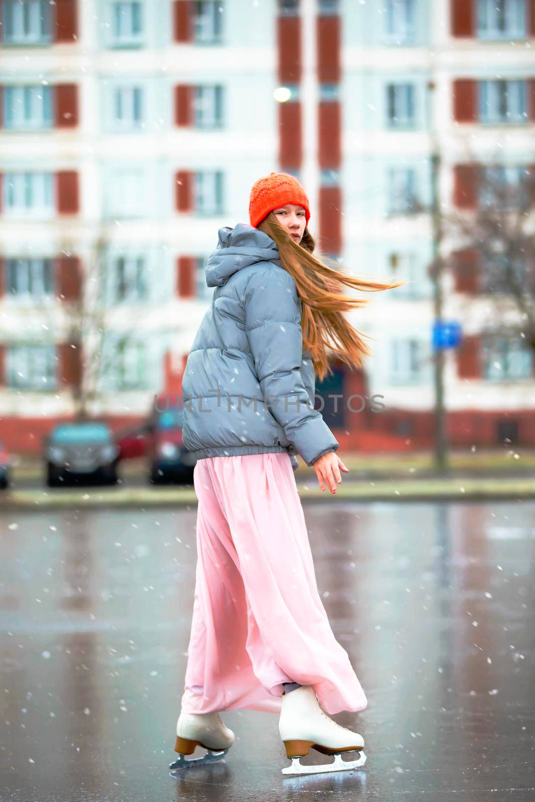 Girl teenager skates on ice in the city.Young girl in a long dress and a warm jacket on the ice.