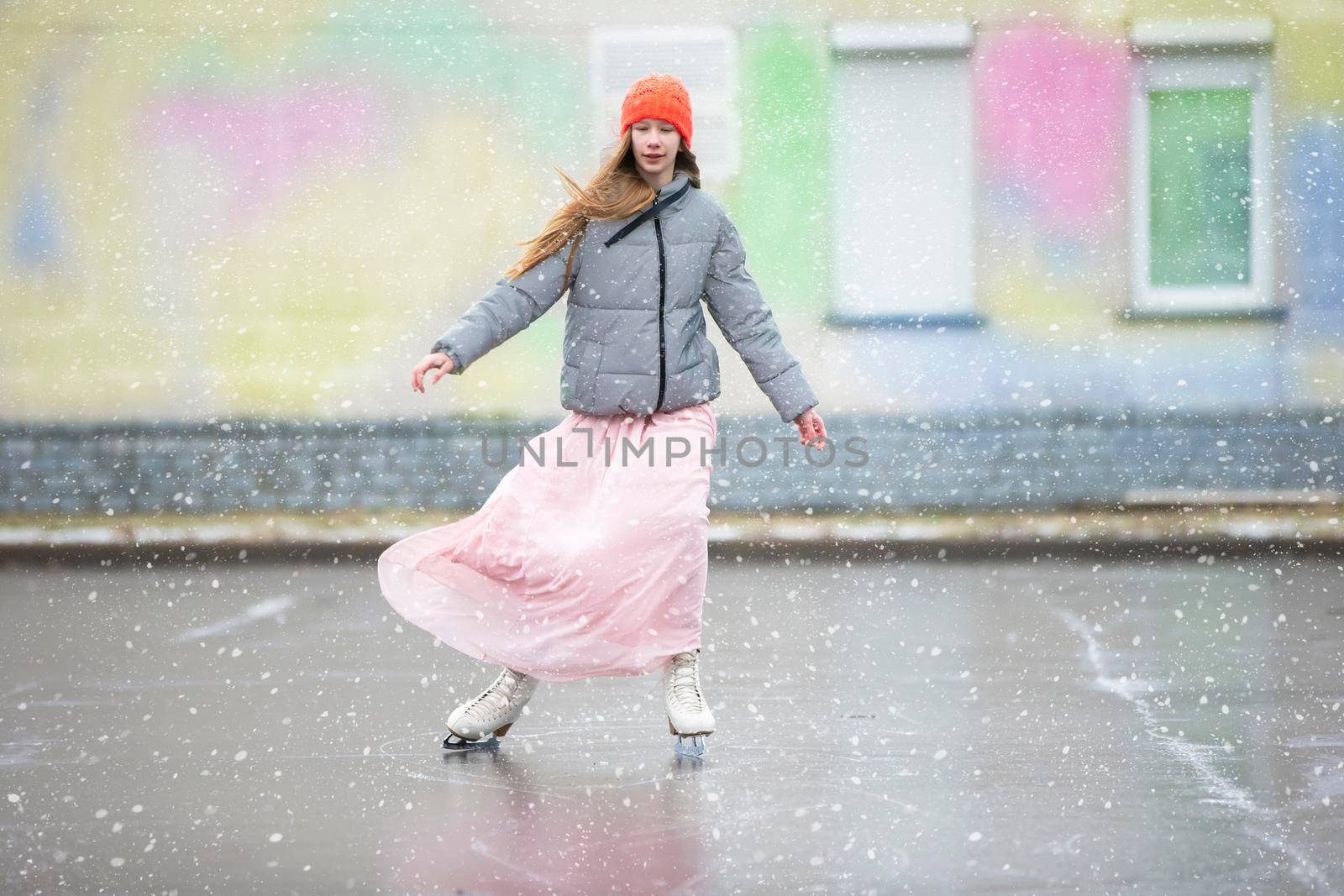 Girl teenager skates on ice in the city.Young girl in a long dress and a warm jacket on the ice.