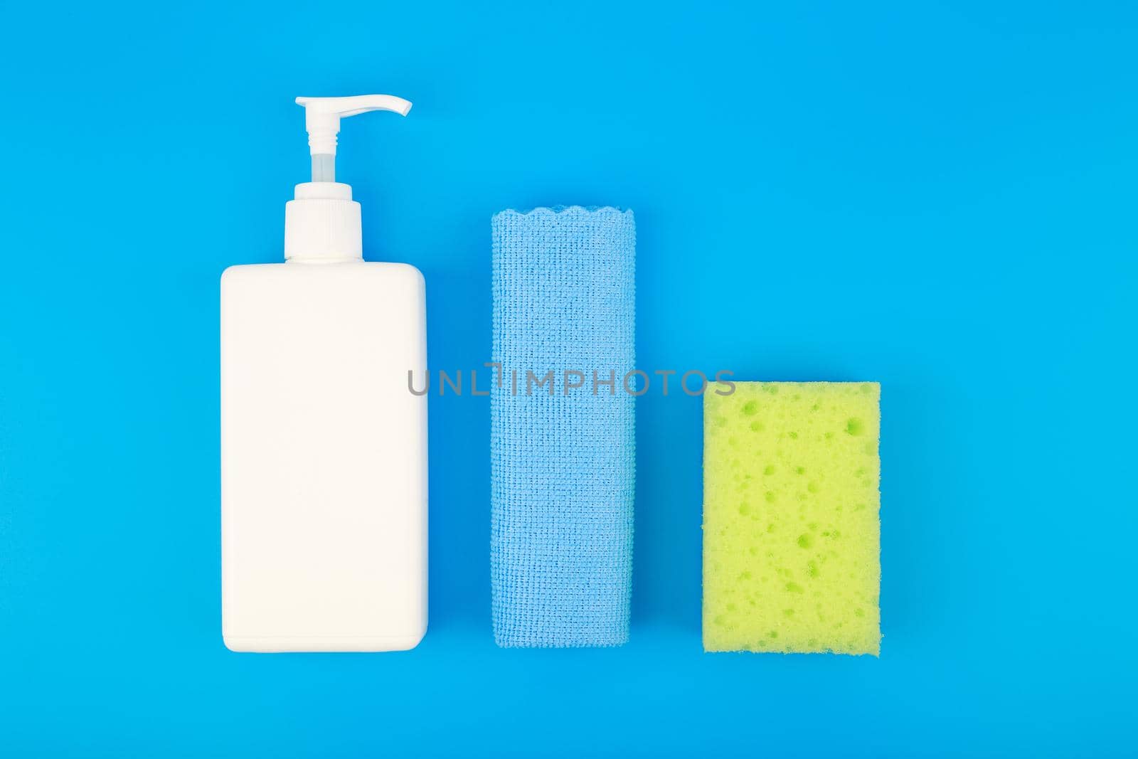 Creative flat lay with detergent in white tube, blue dust cloth and yellow cleaning sponge on blue background. House cleaning and dishwashing concept