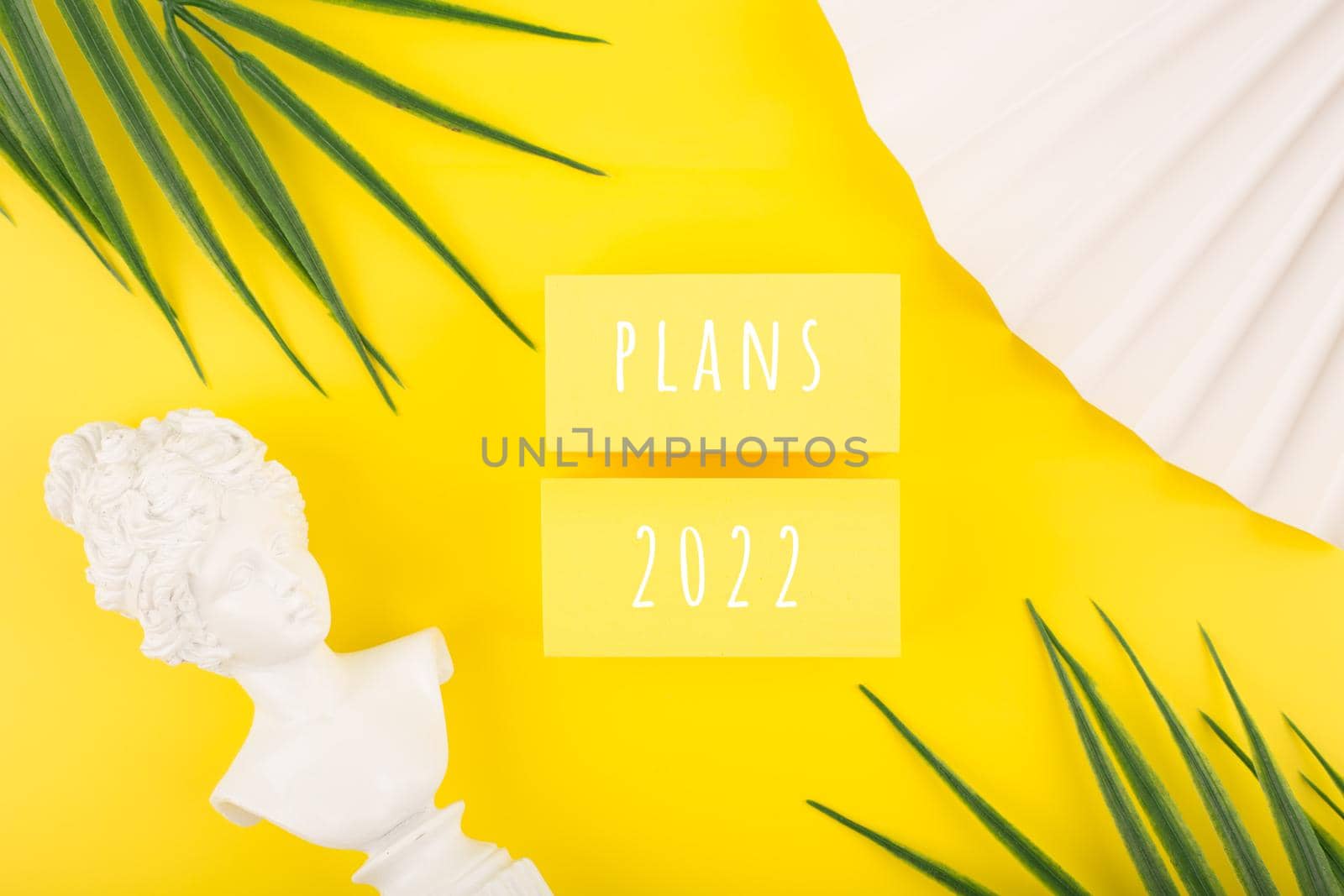 Creative trendy 2022 plans concept. Text written on yellow tablets next to white gypsum woman figure, waver and palm leaves. New year resolution or plans concept