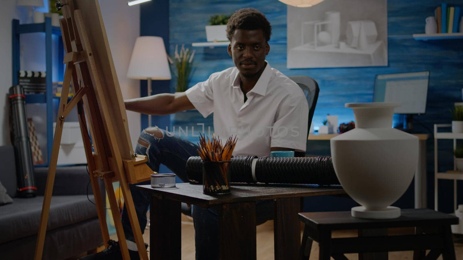 African american person drawing vase design on white canvas in creativity studio. Close up of crafting pencils on table while black young man creating masterpiece in background space