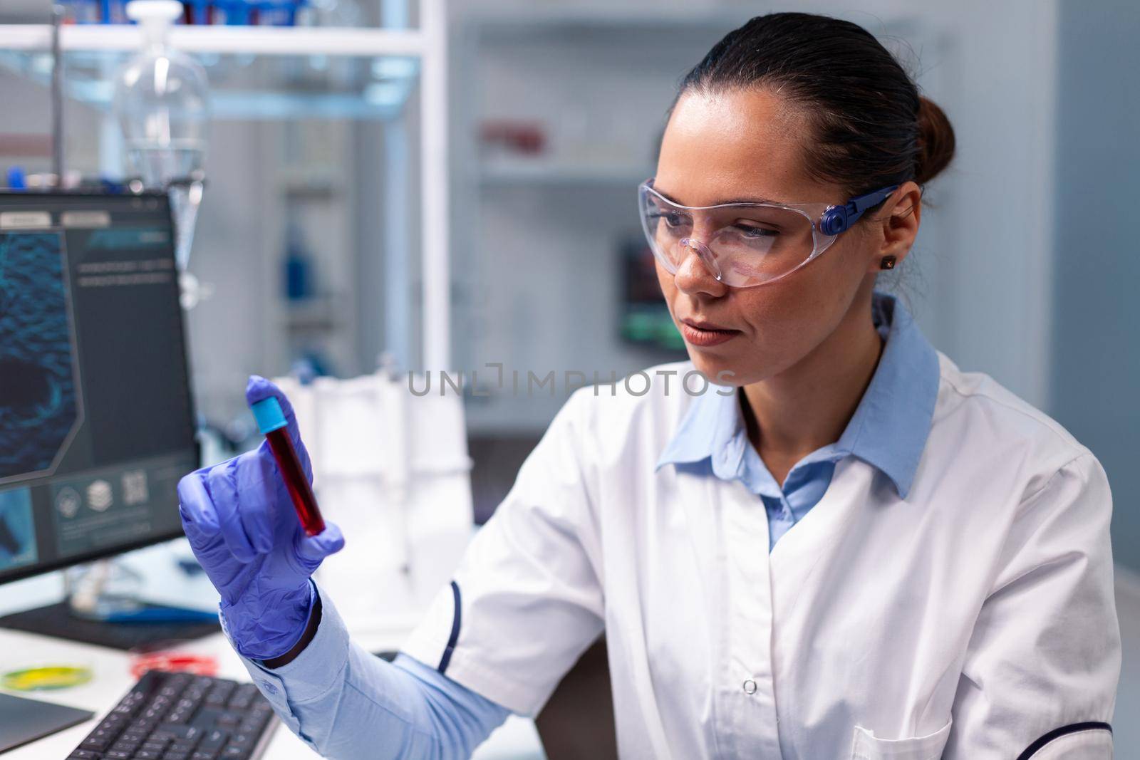Specialist chemist looking at medical vacutainer with blood analyzing microbiology clinical expertise. Researcher woman doctor discovering illness infection working in hospital laboratory