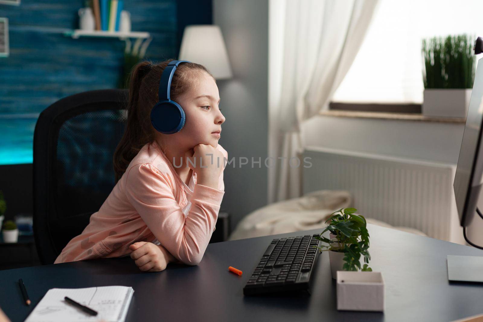 Caucasian student wearing headphones on online class using computer and internet connection at home desk. Smart little child attending elementary school lesson looking at monitor learning