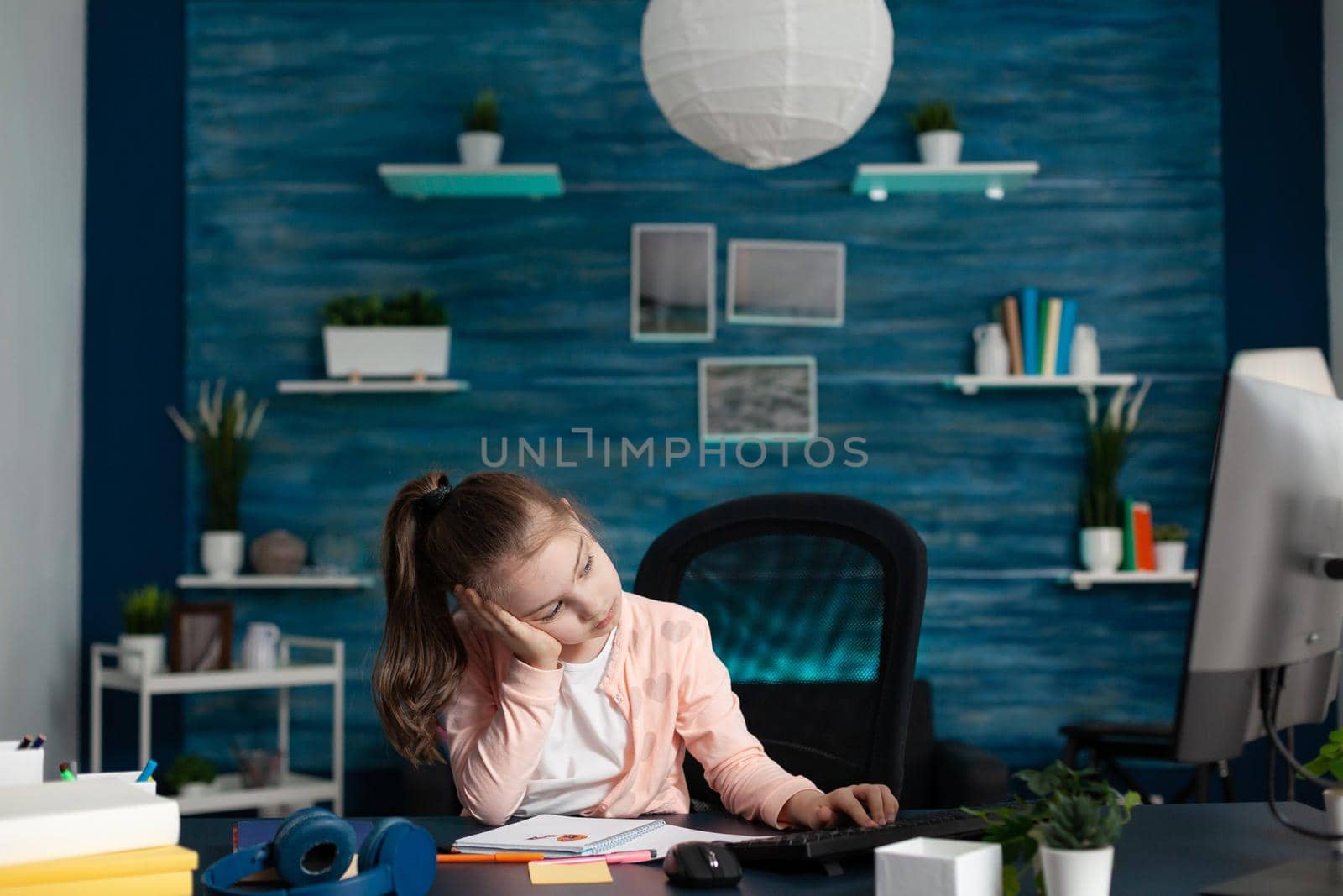 Tired little girl attending online class on internet connection computer at home desk. Exhausted young student from overload homework and studying for knowledge. Overwhelmed schoolgirl