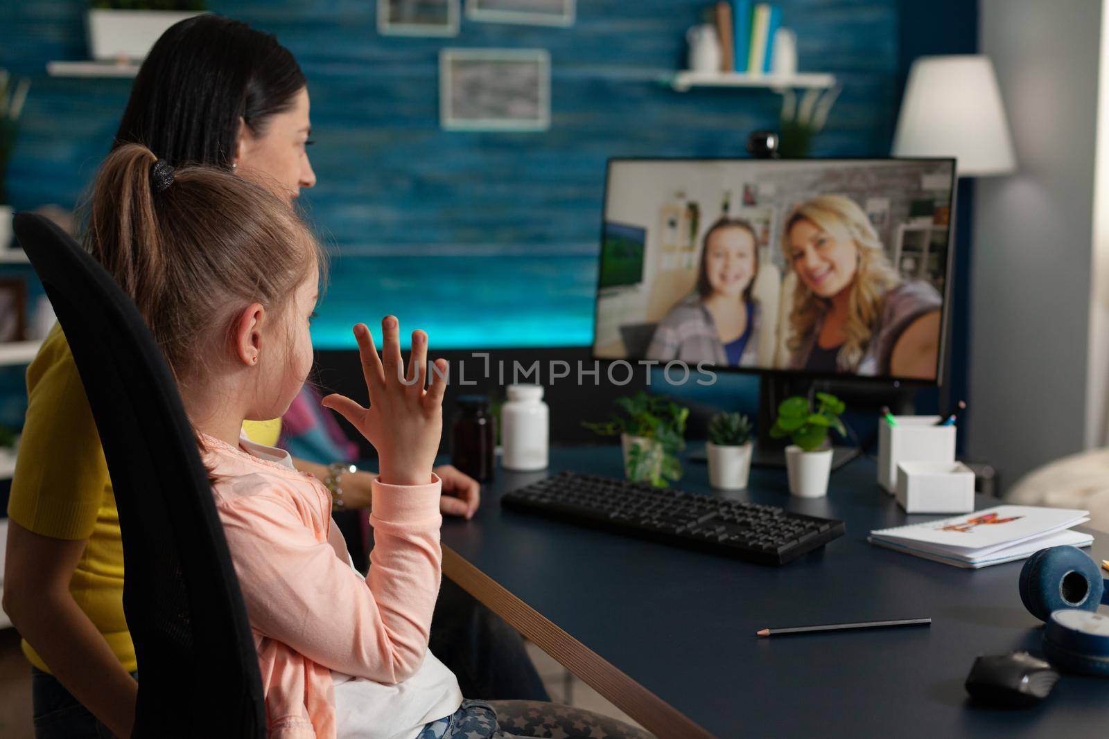 Young child and adult using video call with friends and family while being at home. Mother and daughter on online virtual communication conference computer with cheerful relatives