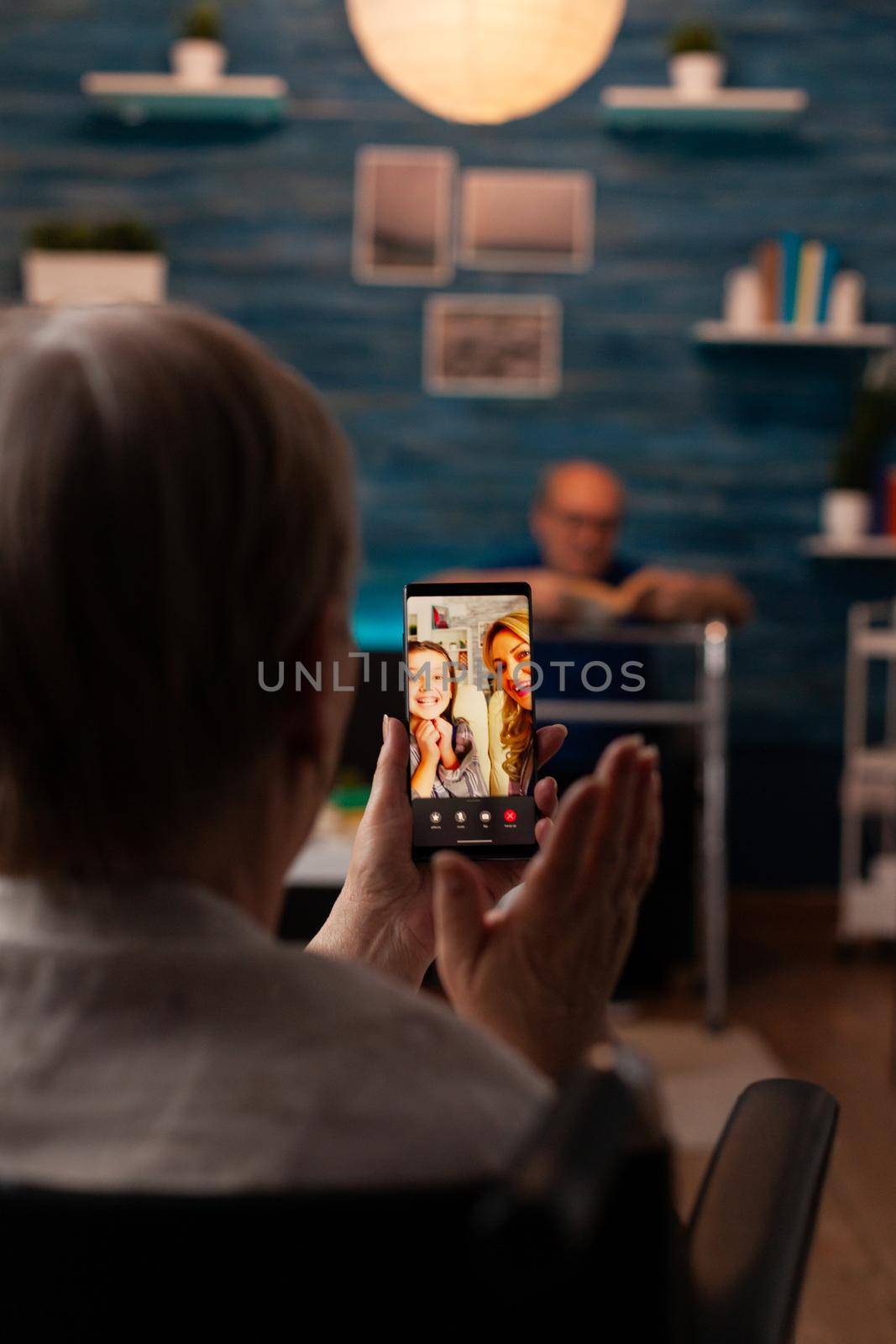 Grandmother talking to family on internet video call using online smartphone technology at home. Retired woman enjoying chat with daughter and niece while sitting in living room with grandfather