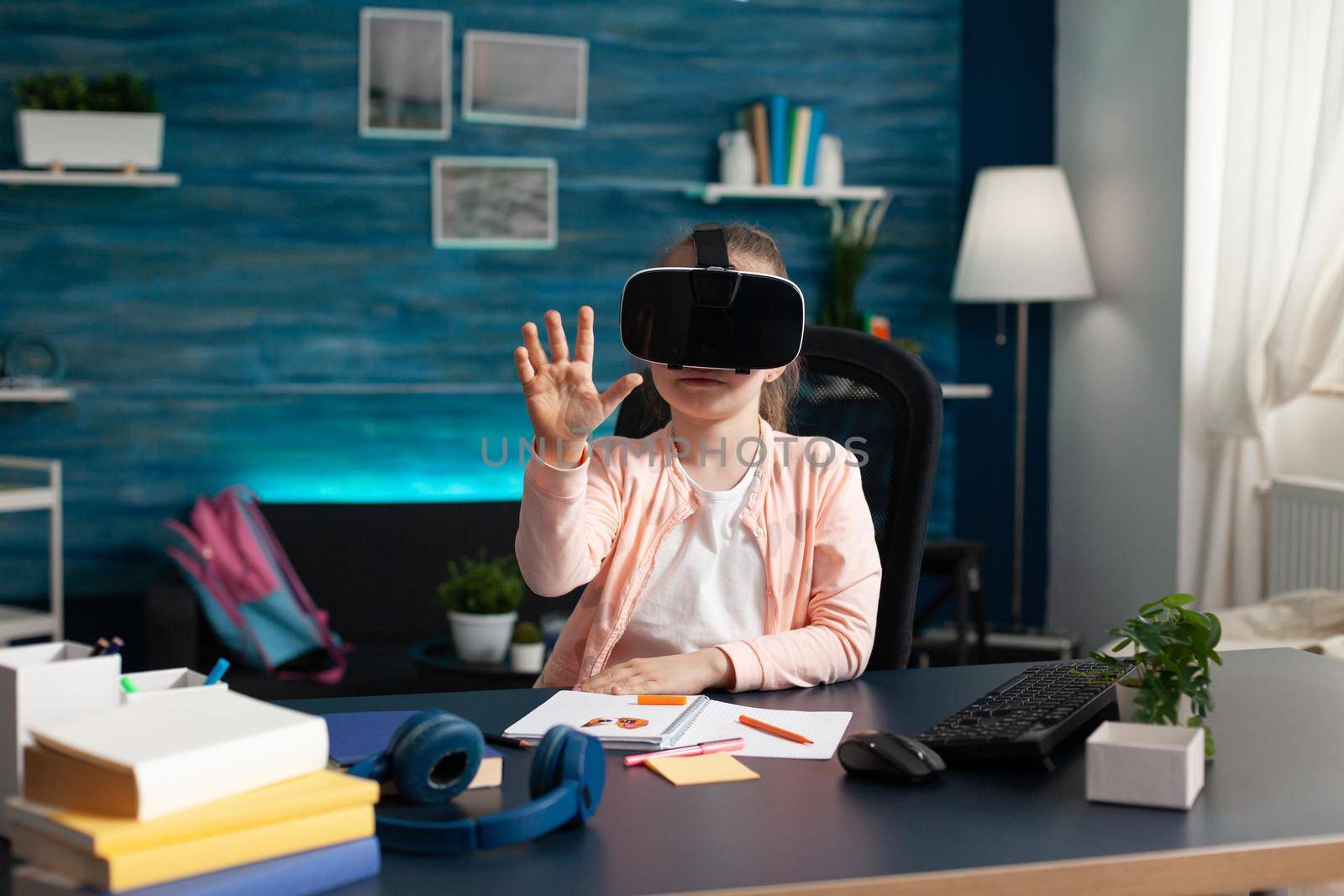 Young child learning lesson course with vr glasses technology gadget at home desk. Smart schoolgirl pupil using vision equipment for elementary school entertainment studying method