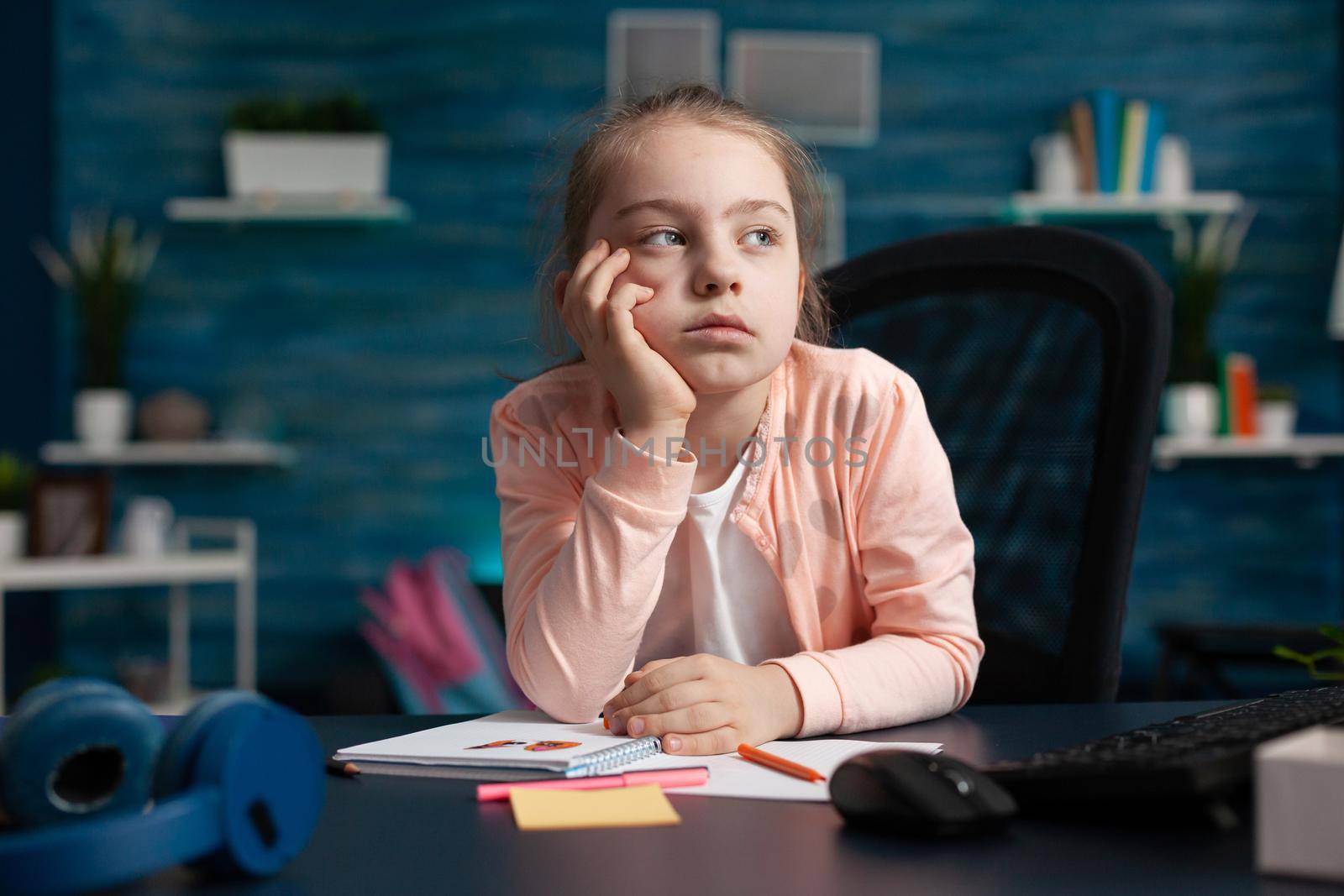 Young student getting online education from home while paying attention to class lesson and notebook paper. Caucasian little girl homeschooled and exhausted from elementary knowledge