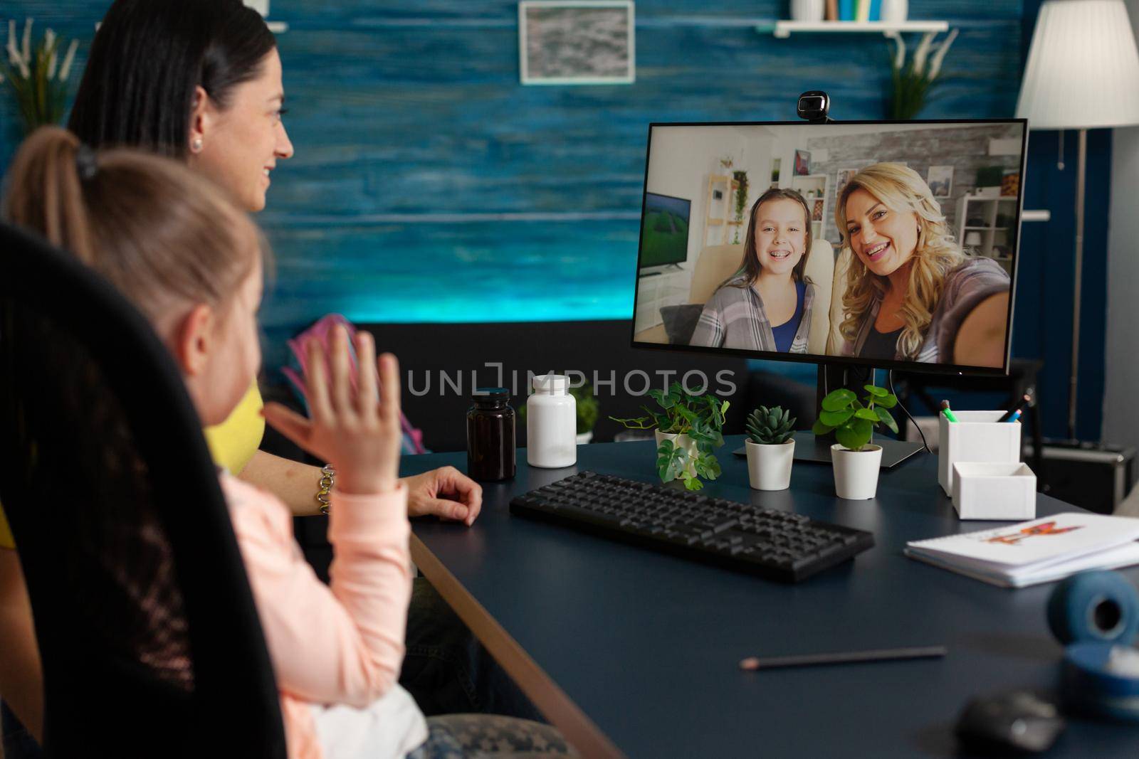 Young child and adult using video call with friends and family while being at home. Mother and daughter on online virtual communication conference computer with cheerful relatives