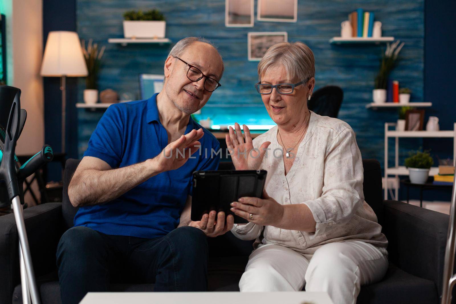 Old husband and wife waving on video call using tablet by DCStudio