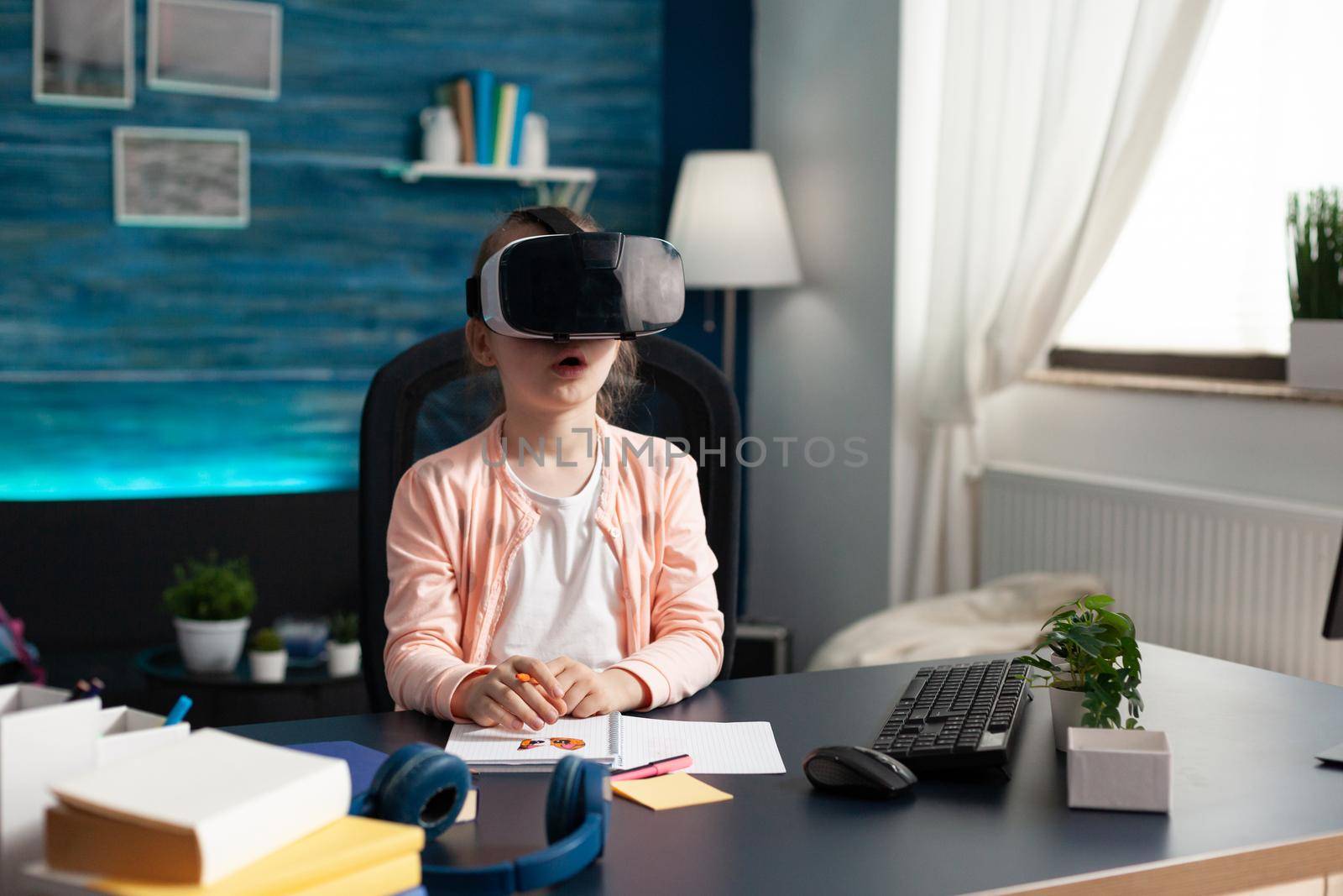 Little pupil at home desk using vr glasses for class lesson studying virtual reality knowledge. Schoolgirl with modern equipment gadget for intelligent learning educational process