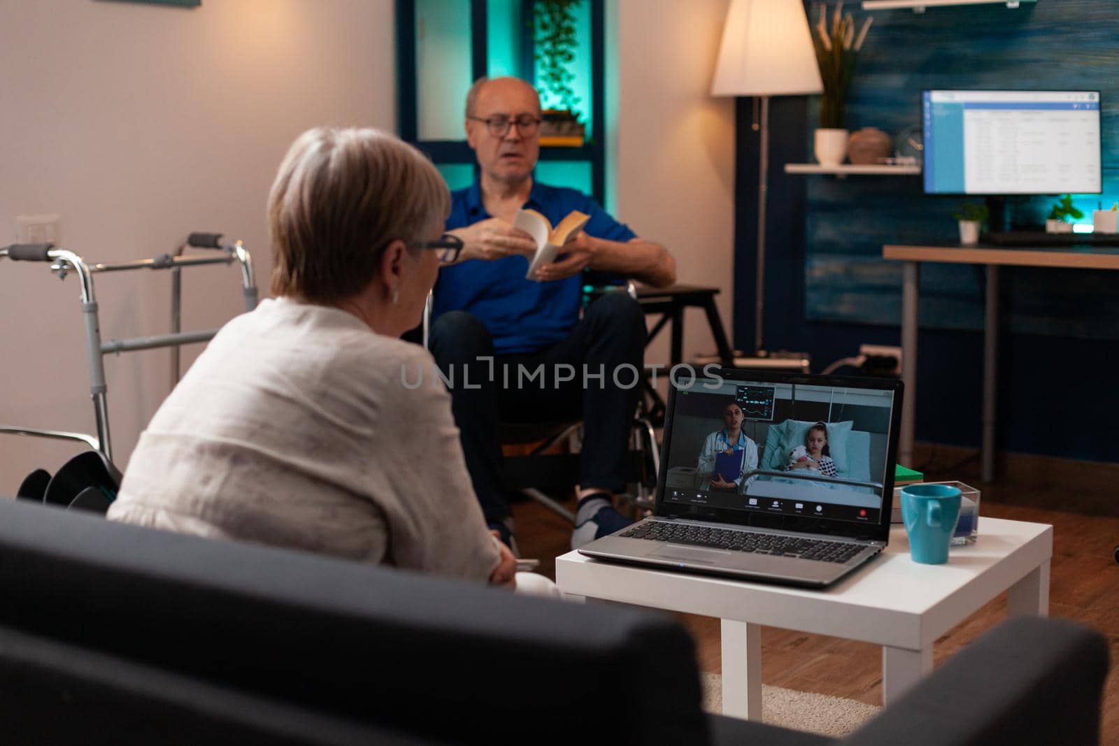 Old grandmother calling doctor in hospital ward clinic to check healthcare diagnosis on video call conference. Woman talking to medic about treatment for niece while man sits in wheelchair