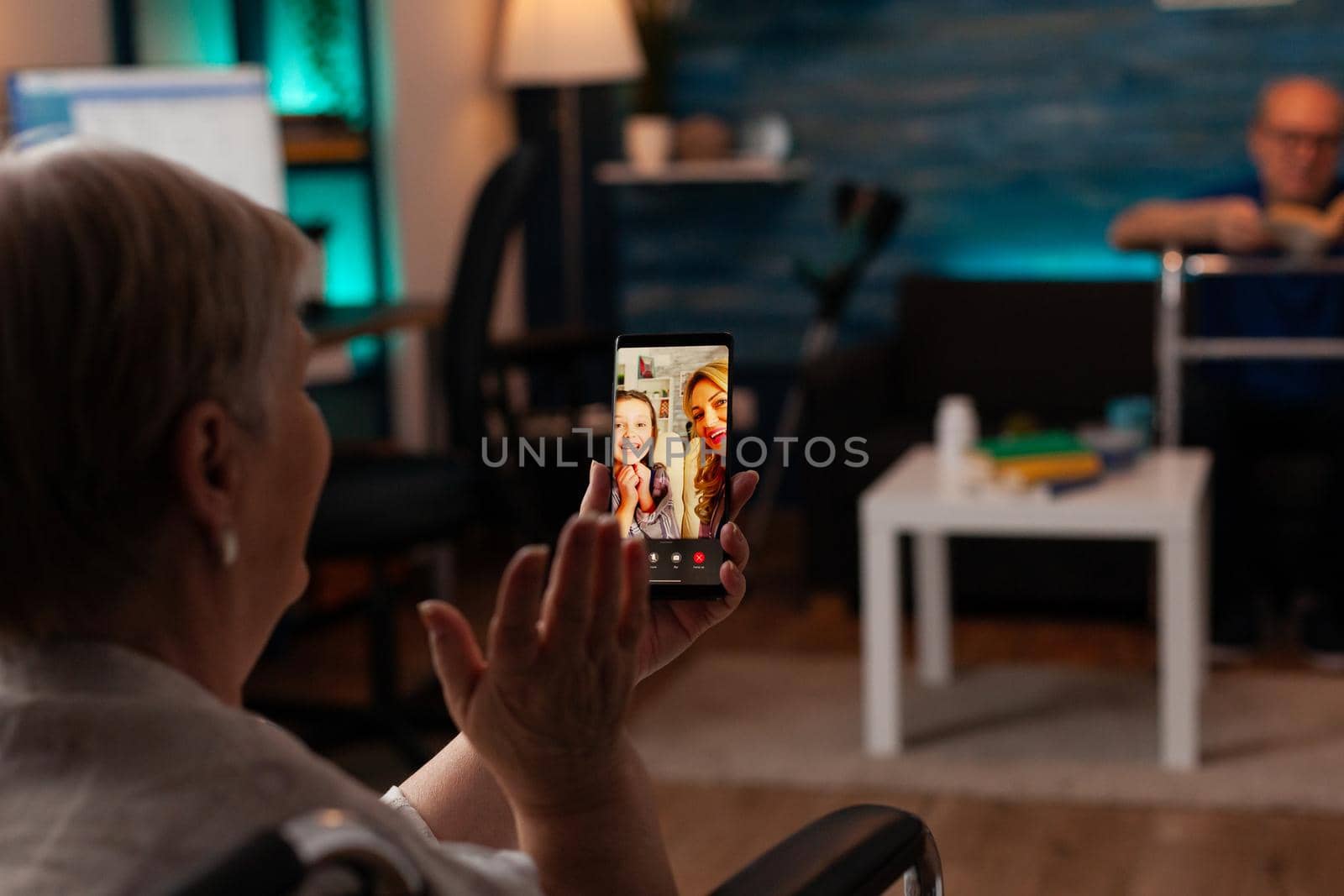 Grandmother talking to family on internet video call using online smartphone technology at home. Retired woman enjoying chat with daughter and niece while sitting in living room with grandfather
