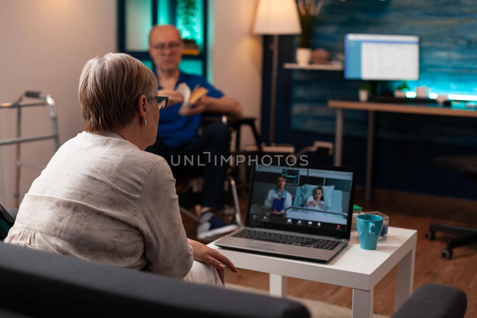 Old grandmother calling doctor in hospital ward clinic to check healthcare diagnosis on video call conference. Woman talking to medic about treatment for niece while man sits in wheelchair